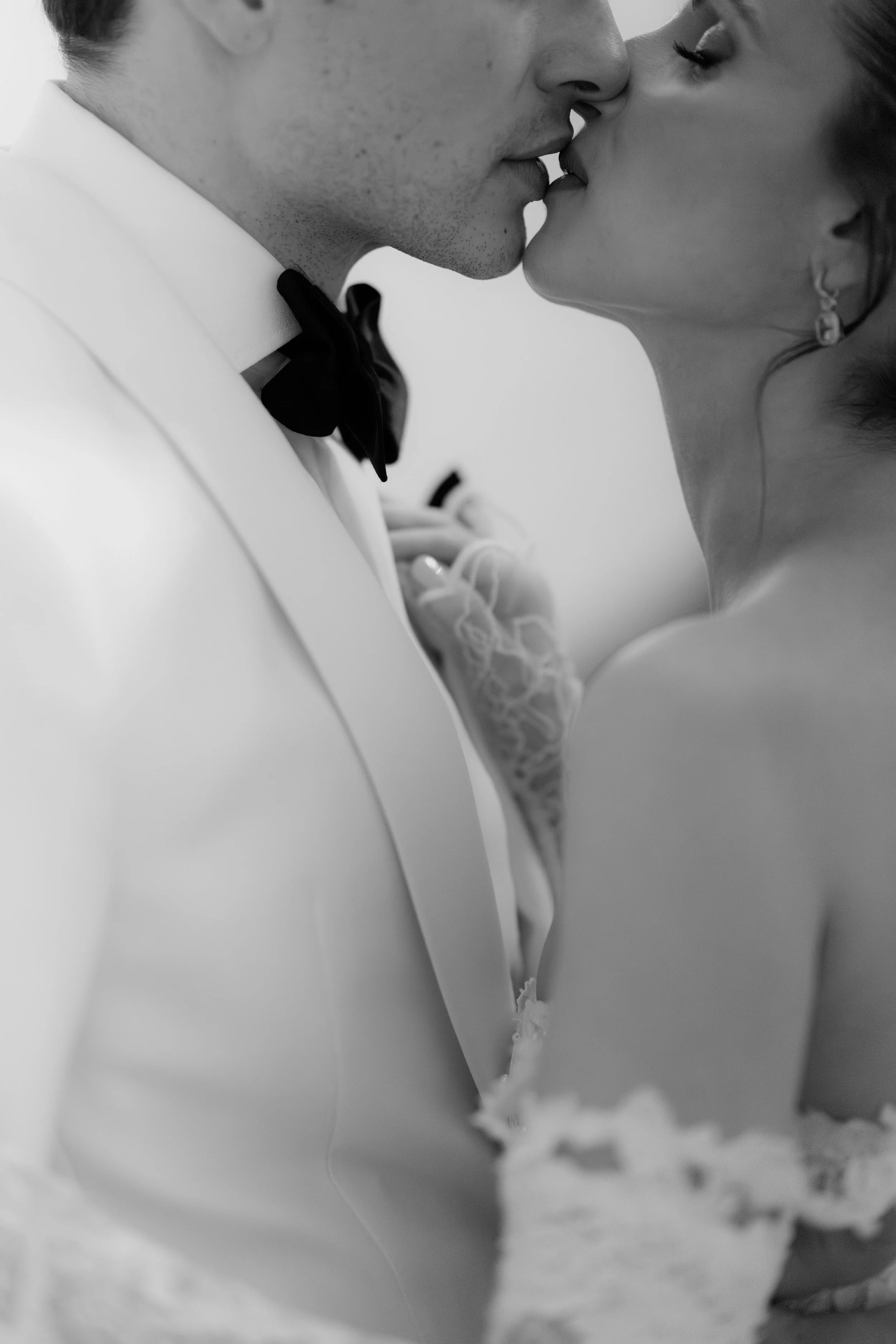 A black and white close-up photo of a couple about to kiss, wearing satin and lace wedding attire.