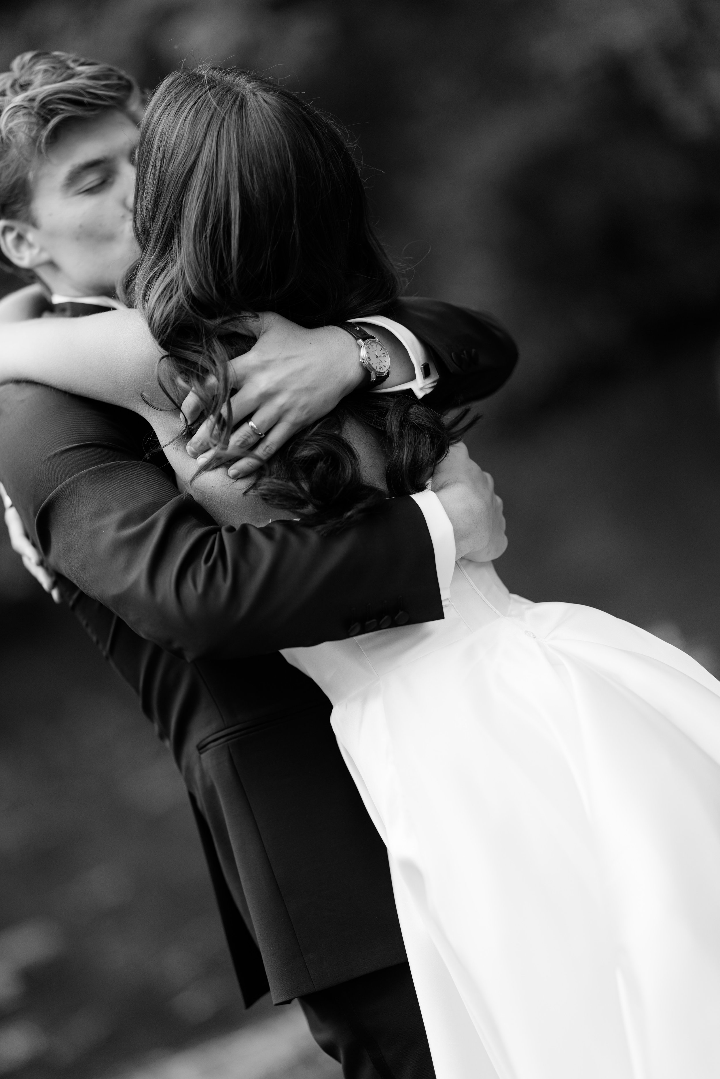 A couple sharing a passionate embrace outdoors, with the woman's face hidden and the man appearing to kiss her cheek.