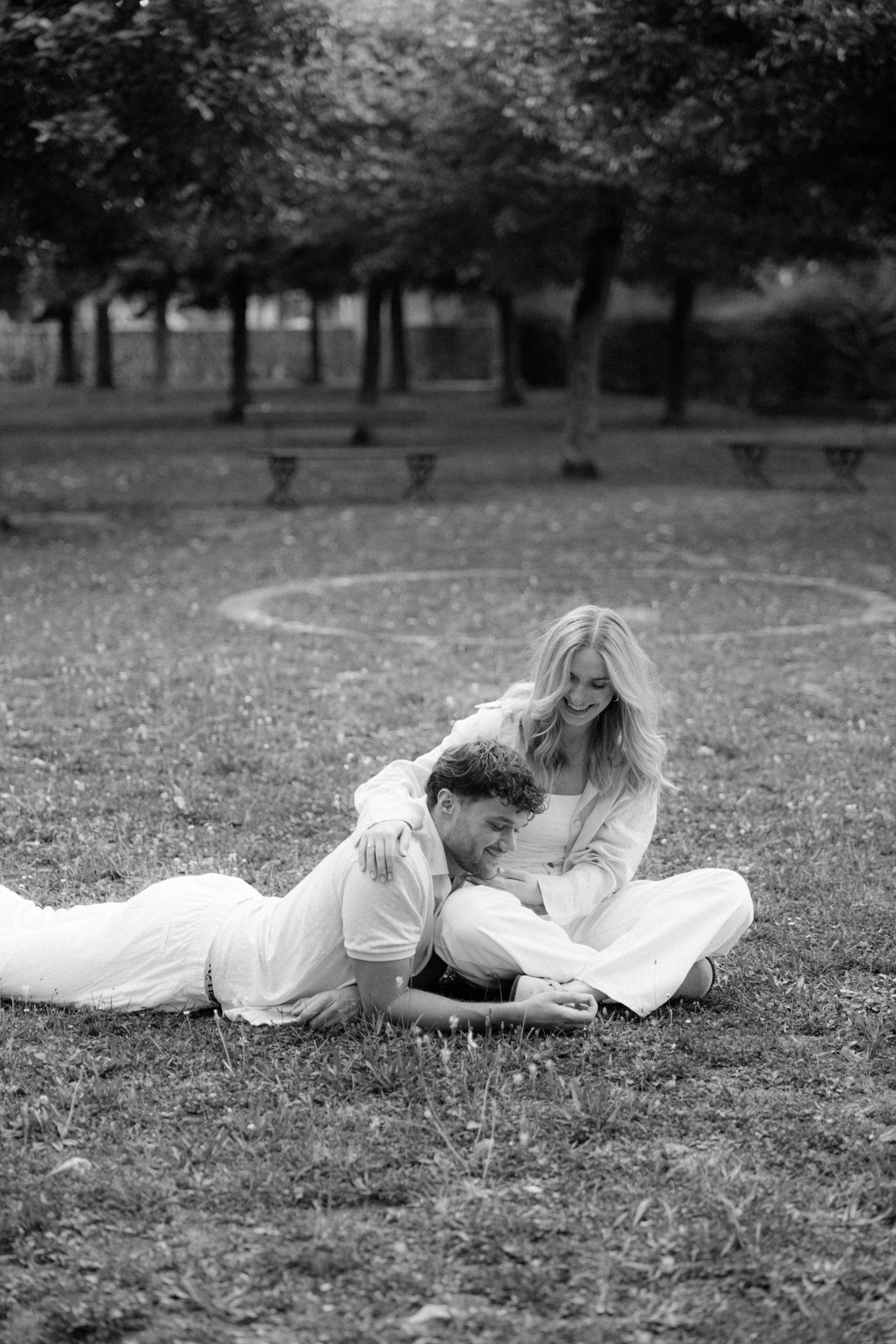 A man and woman are lying on the grass in a park, smiling and enjoying each other's company.