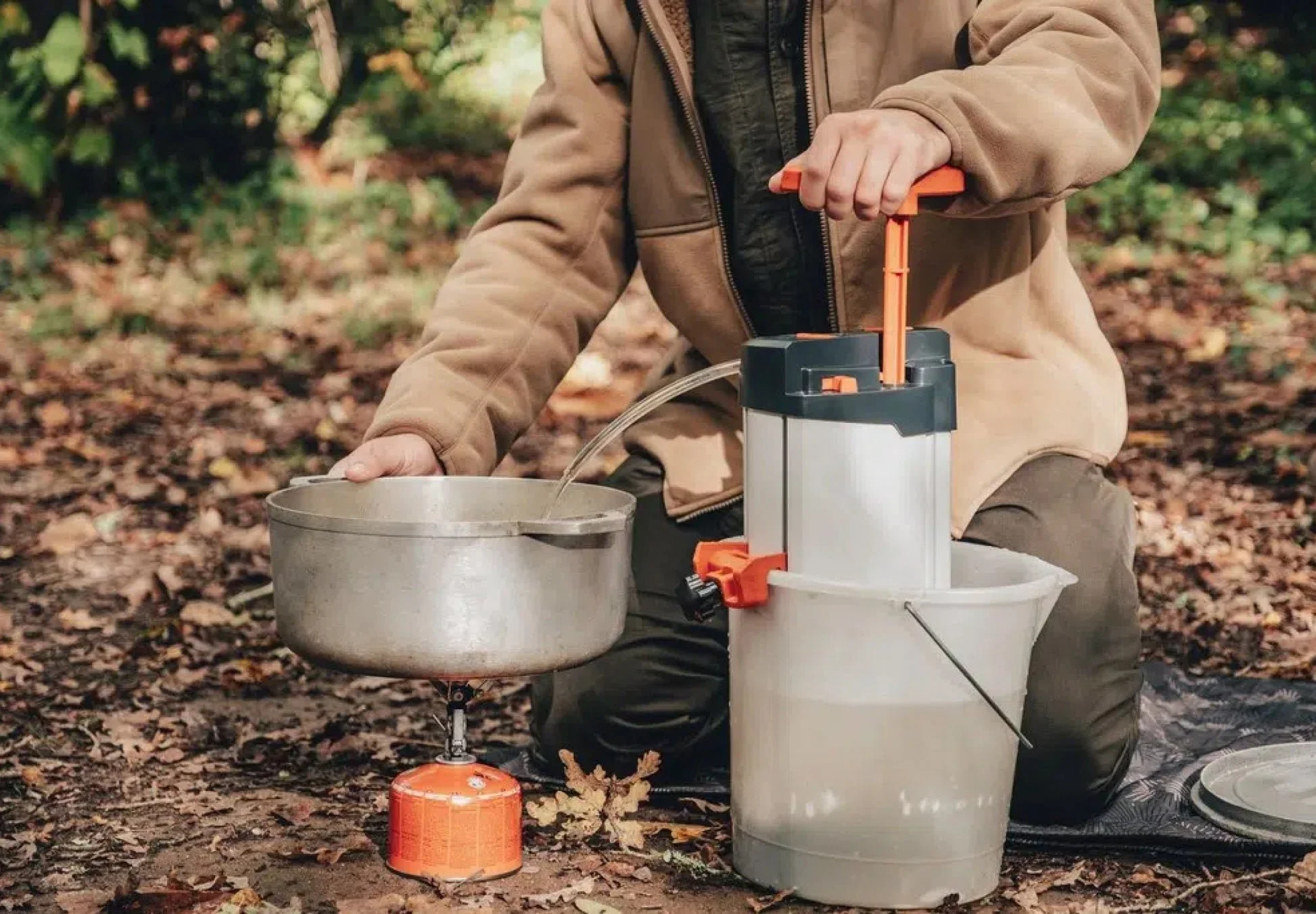 Une personne en pleine nature, en forêt, utilisant un extracteur de sève d'érable au sol pour récolter la sève dans un récipient.
