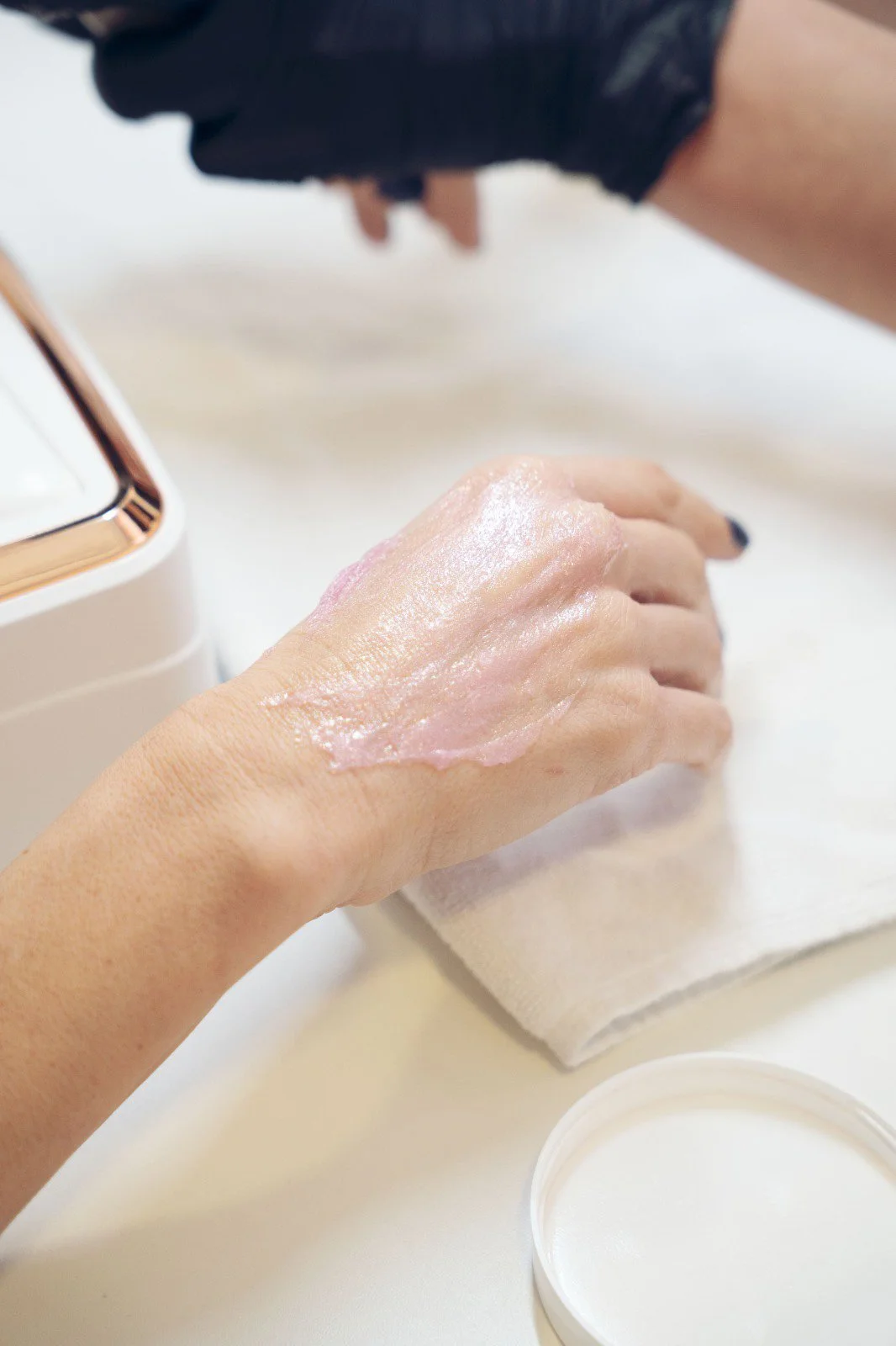 Mano che applica una maschera cosmetica sulla pelle della mano in un ambiente luminoso.