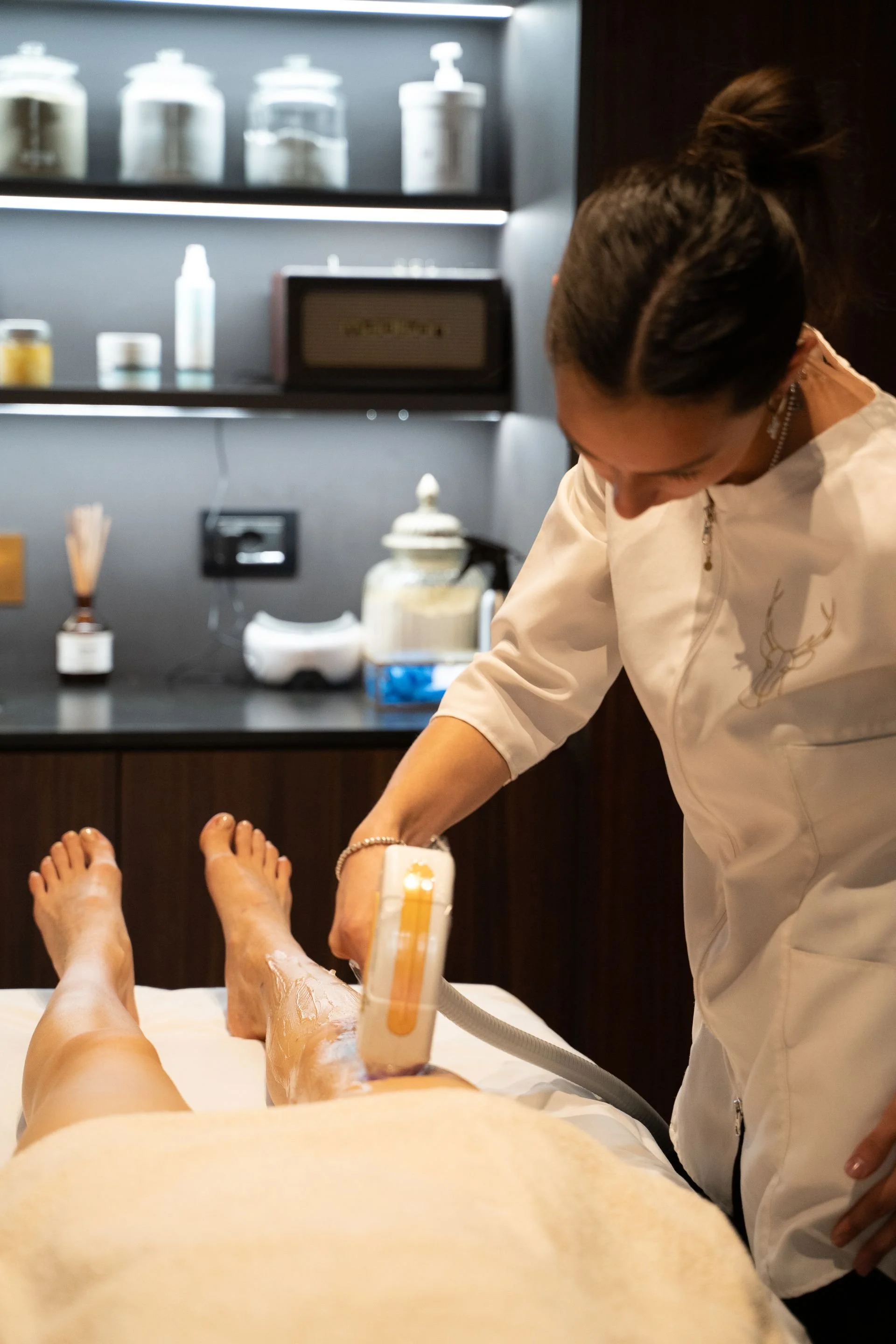 Estetista che esegue una terapia con dispositivo a LED sulla gamba di una paziente in un centro benessere o salone estetico.