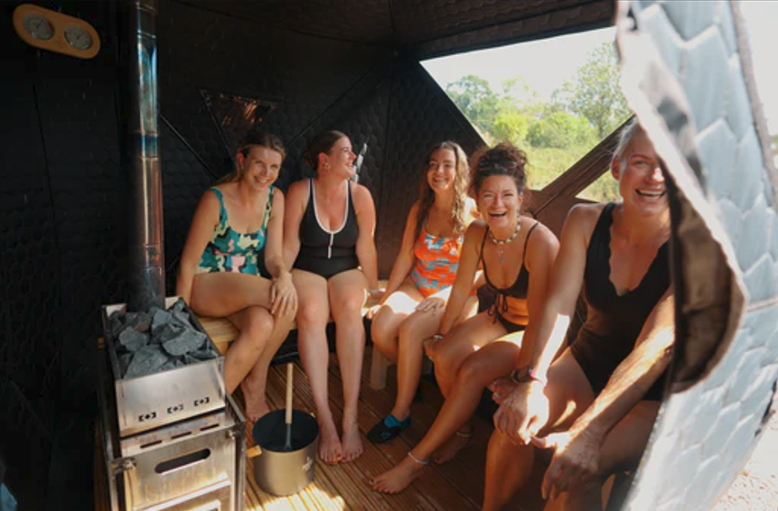 Five women sitting inside a sauna, smiling and laughing together.