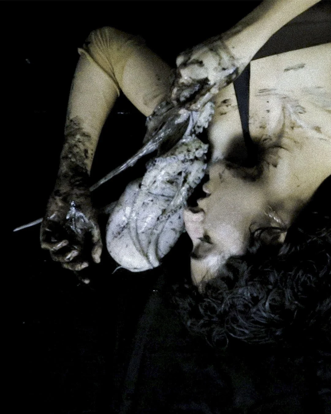 A person lying on a dark floor, dragging an octopus across their chest by the tentacles. 