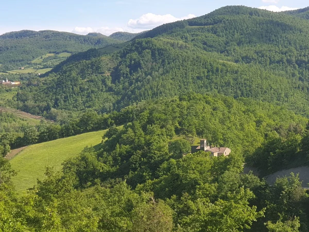 Green mountainous landscape with a large monastery house, with a bell tower among trees in a valley in Italy.