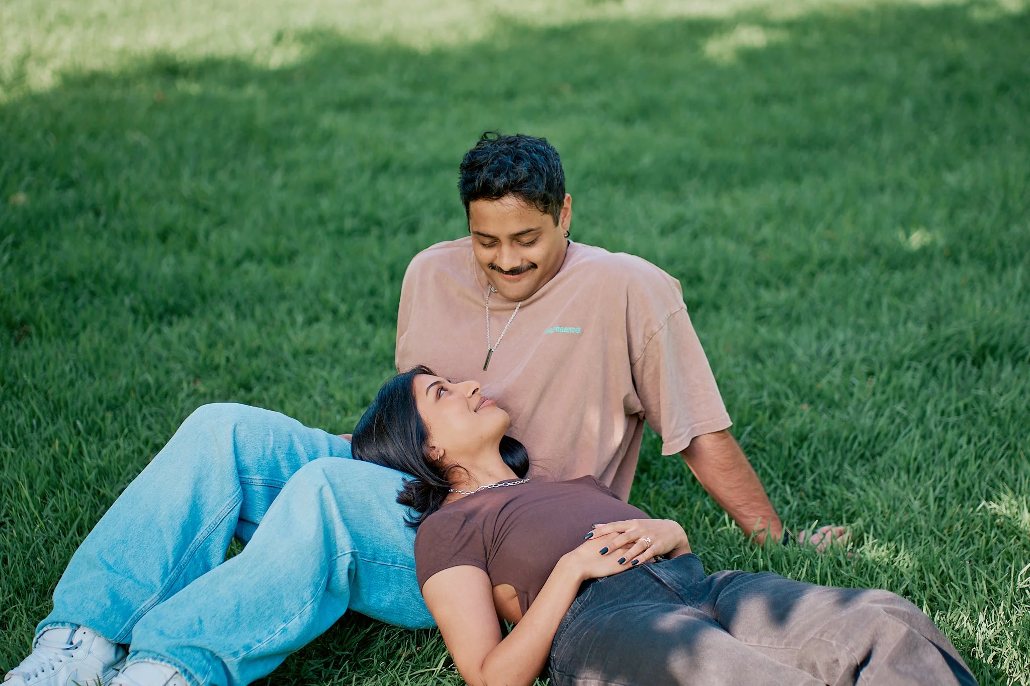 A man and woman sitting on grass, gazing at each other lovingly.