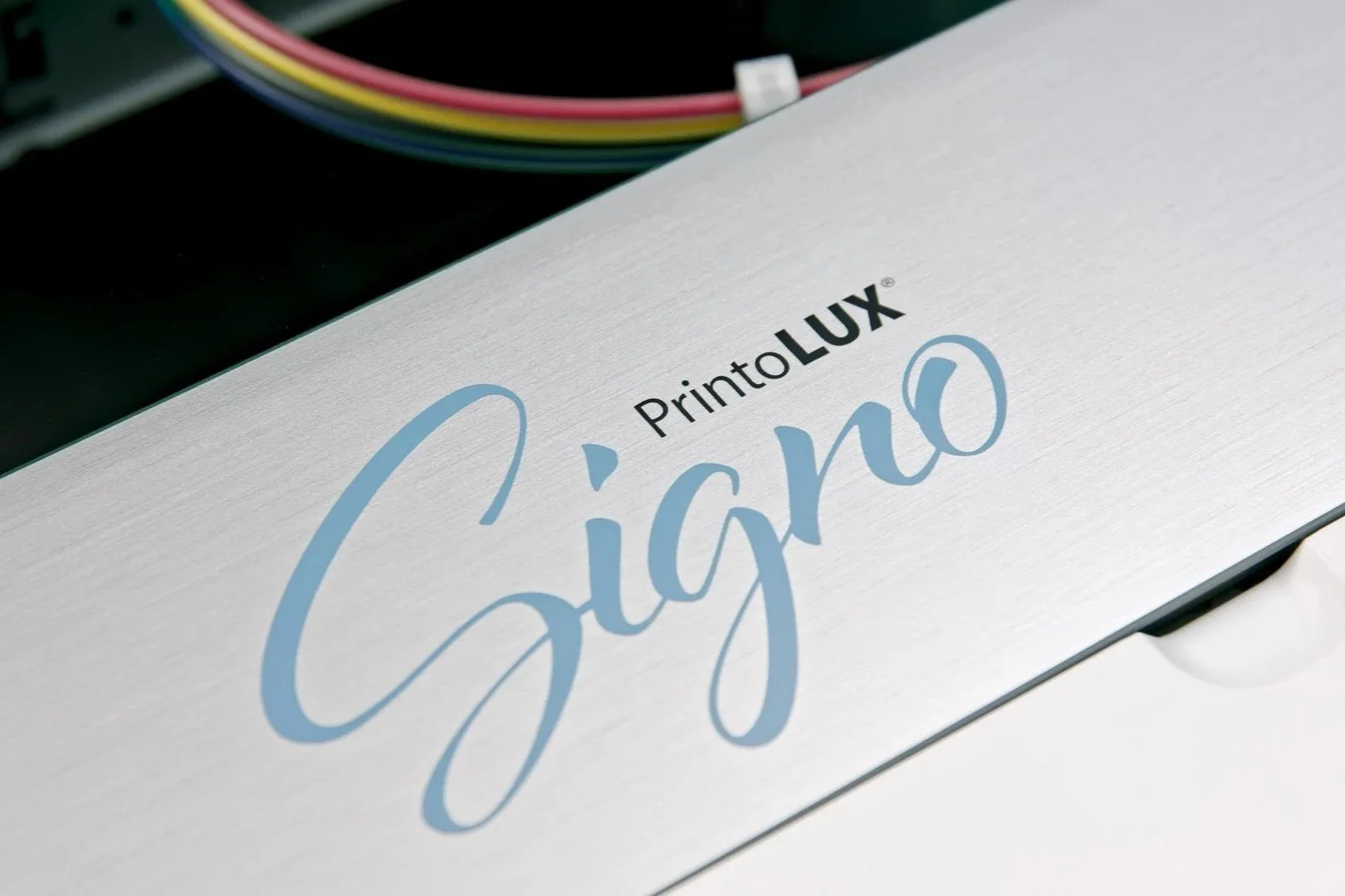 Close-up of a white box with black and blue text that reads "PrintoLUX Signo" and part of a multicolored cable in the background.
