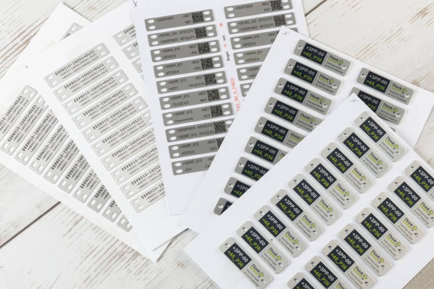 Sheets of Printolux electronic label tags with barcodes and text, some with green and black branding, on a white wooden surface.