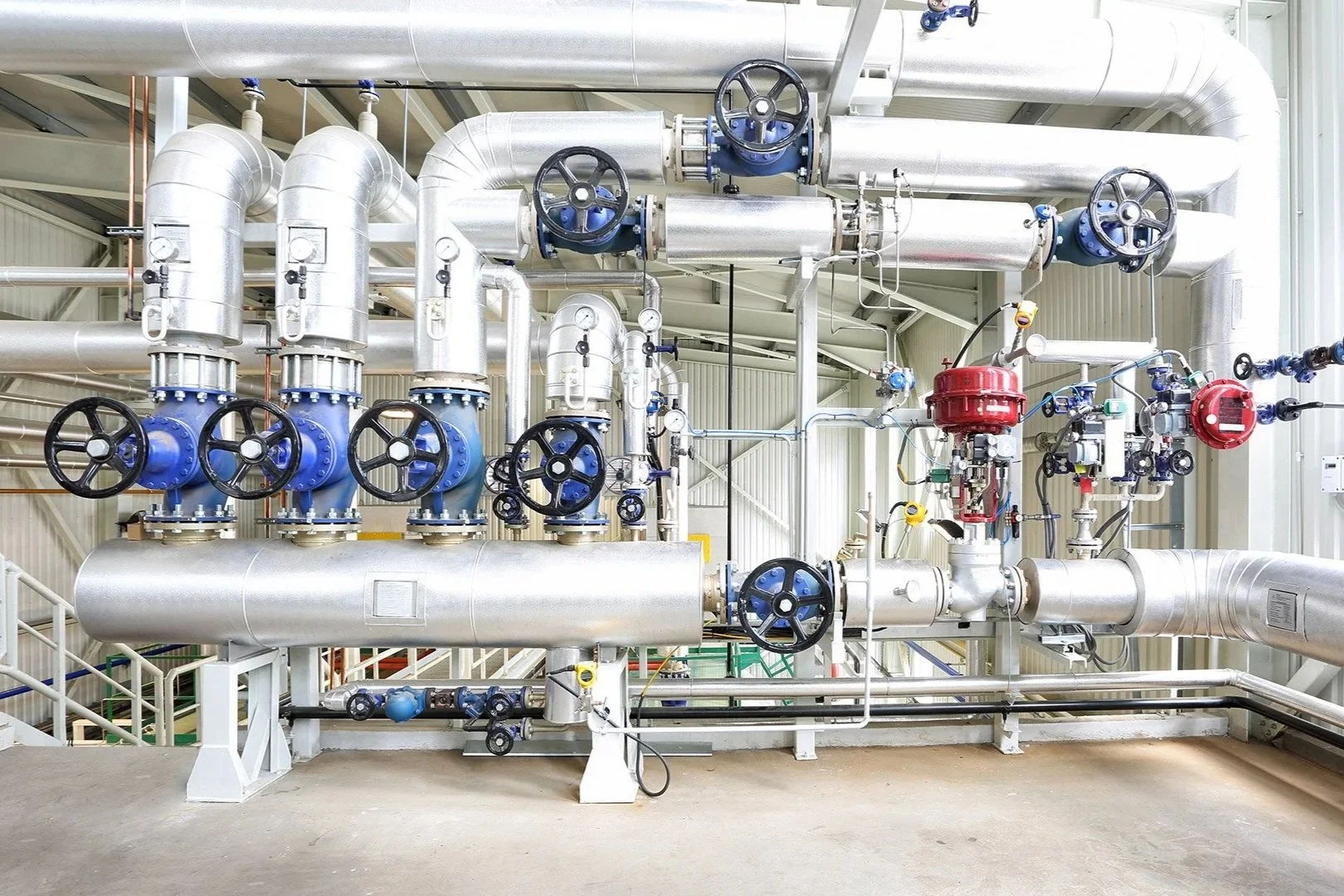 Industrial piping system with metallic pipes, blue valves, and gauges inside a factory or plant.