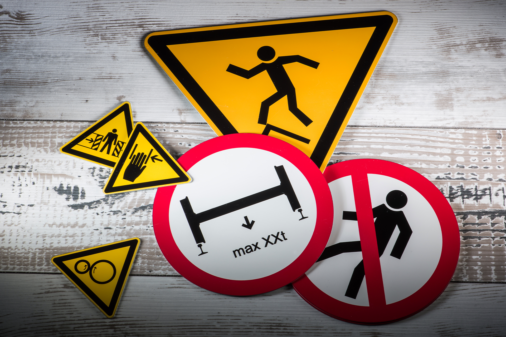 A collection of various printolux printed caution and warning signs on a wooden surface, including signs for construction, hazard, and no pedestrian entry.