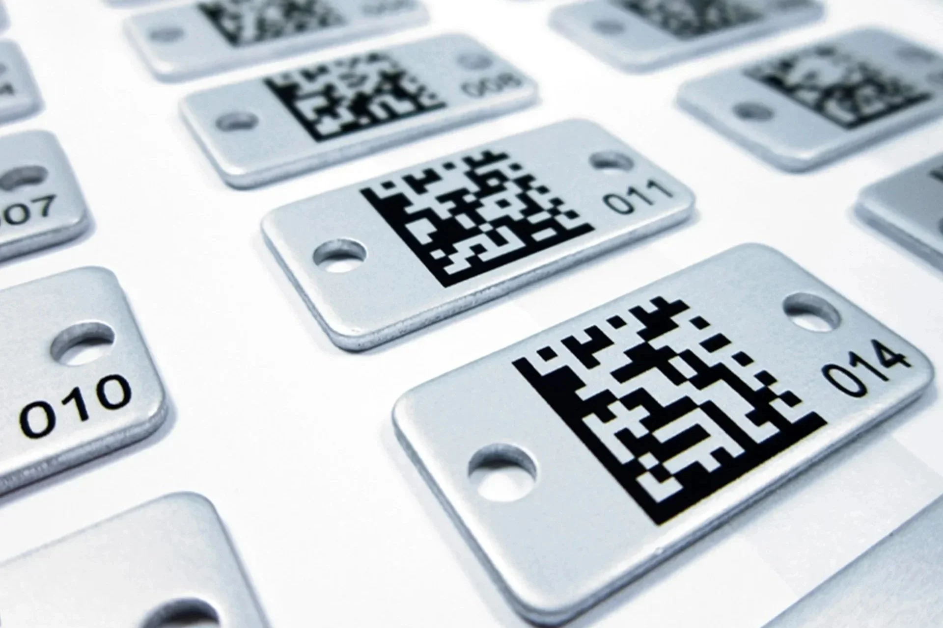 Close-up of aluminium PrintoLUX tags, each labeled with a QR code and a number, used for electronic voting or identification.