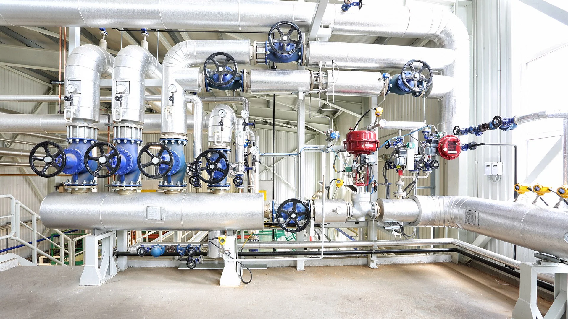 Industrial piping system with metallic pipes, blue valves, and gauges inside a factory or plant.