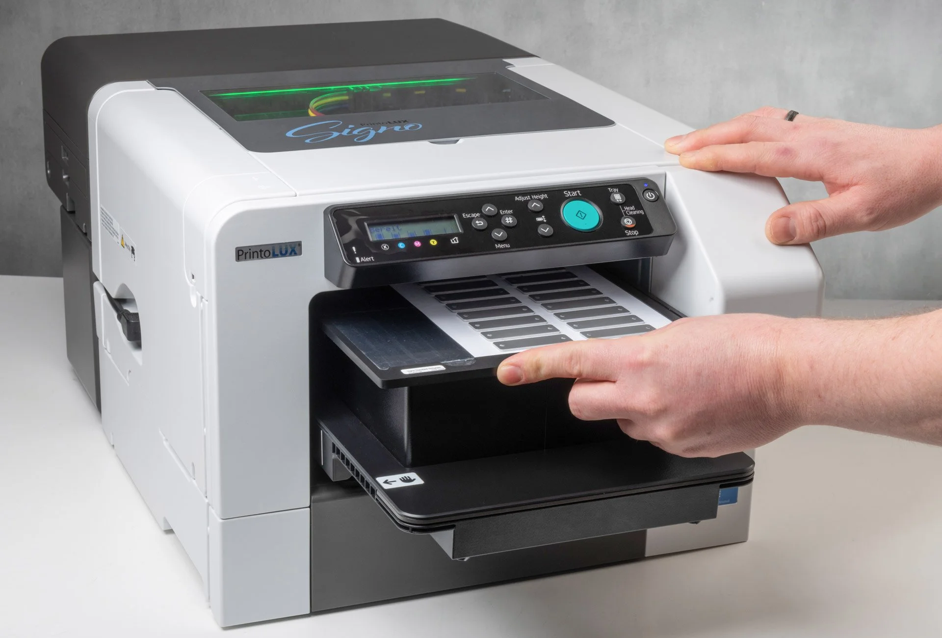 A person operates the Printolux Signo printer with a page of materials and control panel, printing small metals tags for cables.