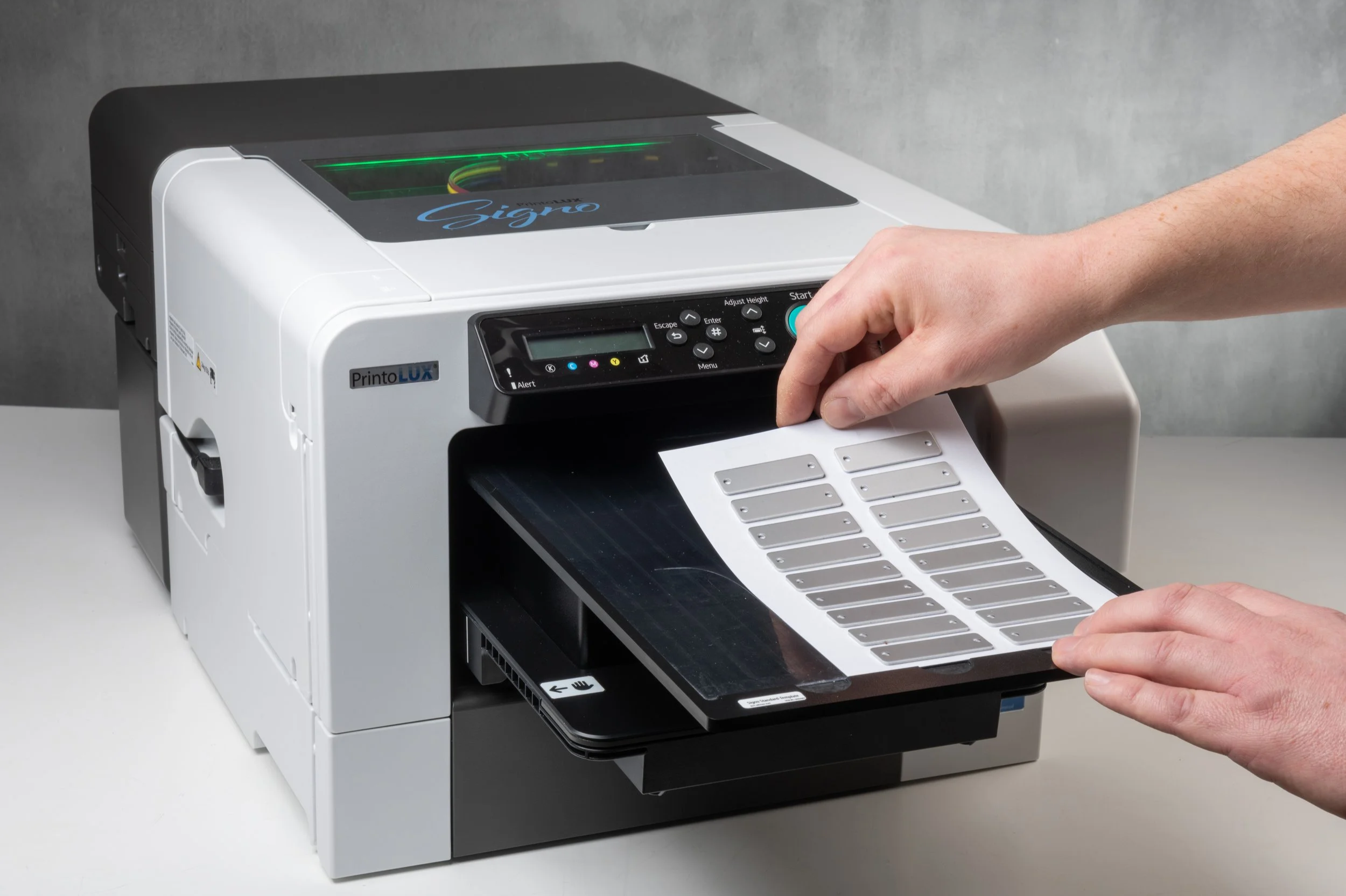 A person operating a Signo PrintoLUX industrial printer, feeding metal labels into the machine for printing or labeling.