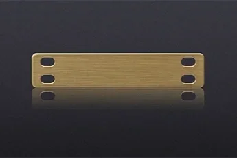 A brass or gold-colored metal bracket or mounting strip with multiple elongated oval holes on a black reflective surface.