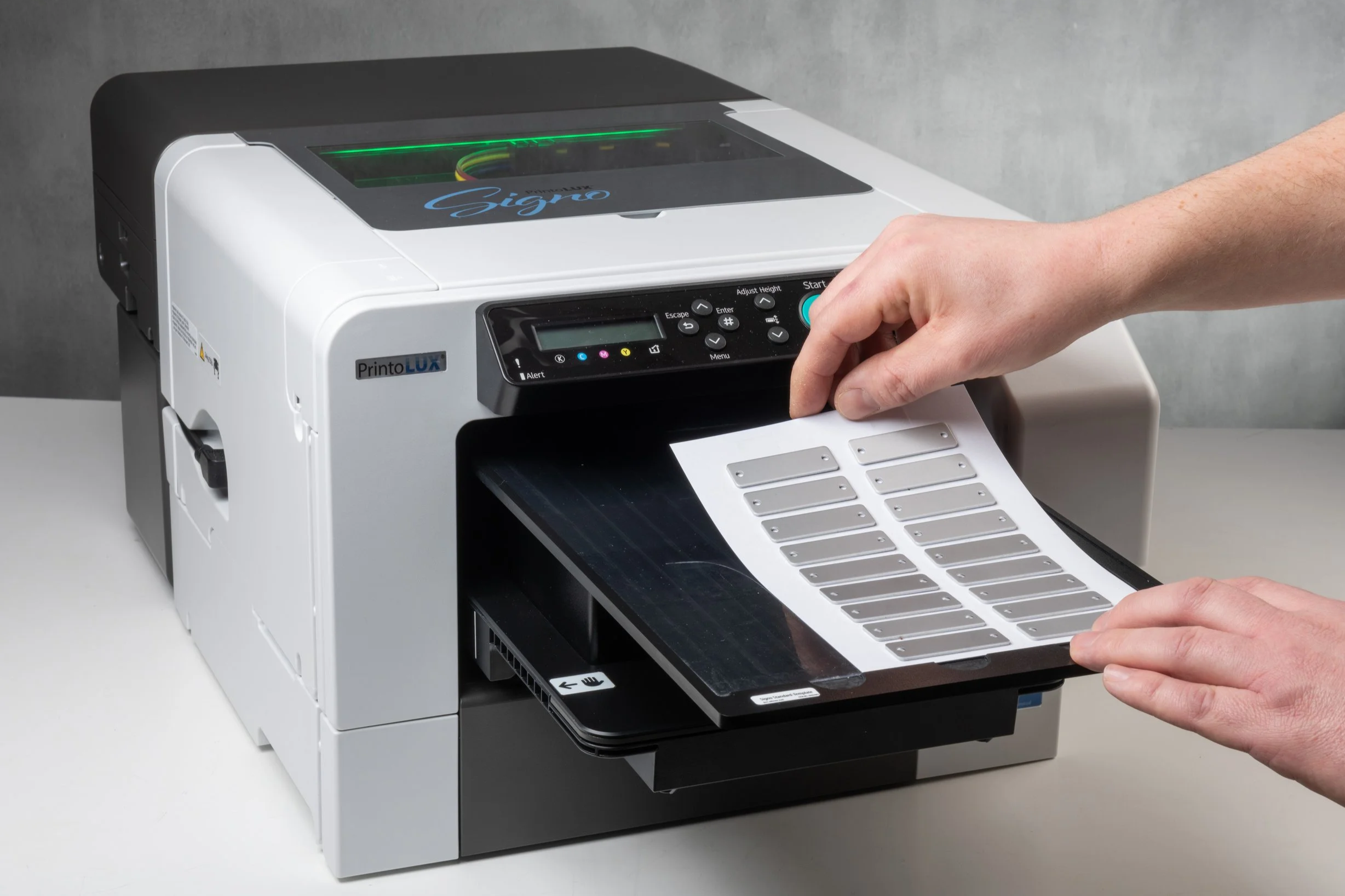 A person operating the Printolux Signo machine. Loading a sheet of small metal cable tags onto the print bed.