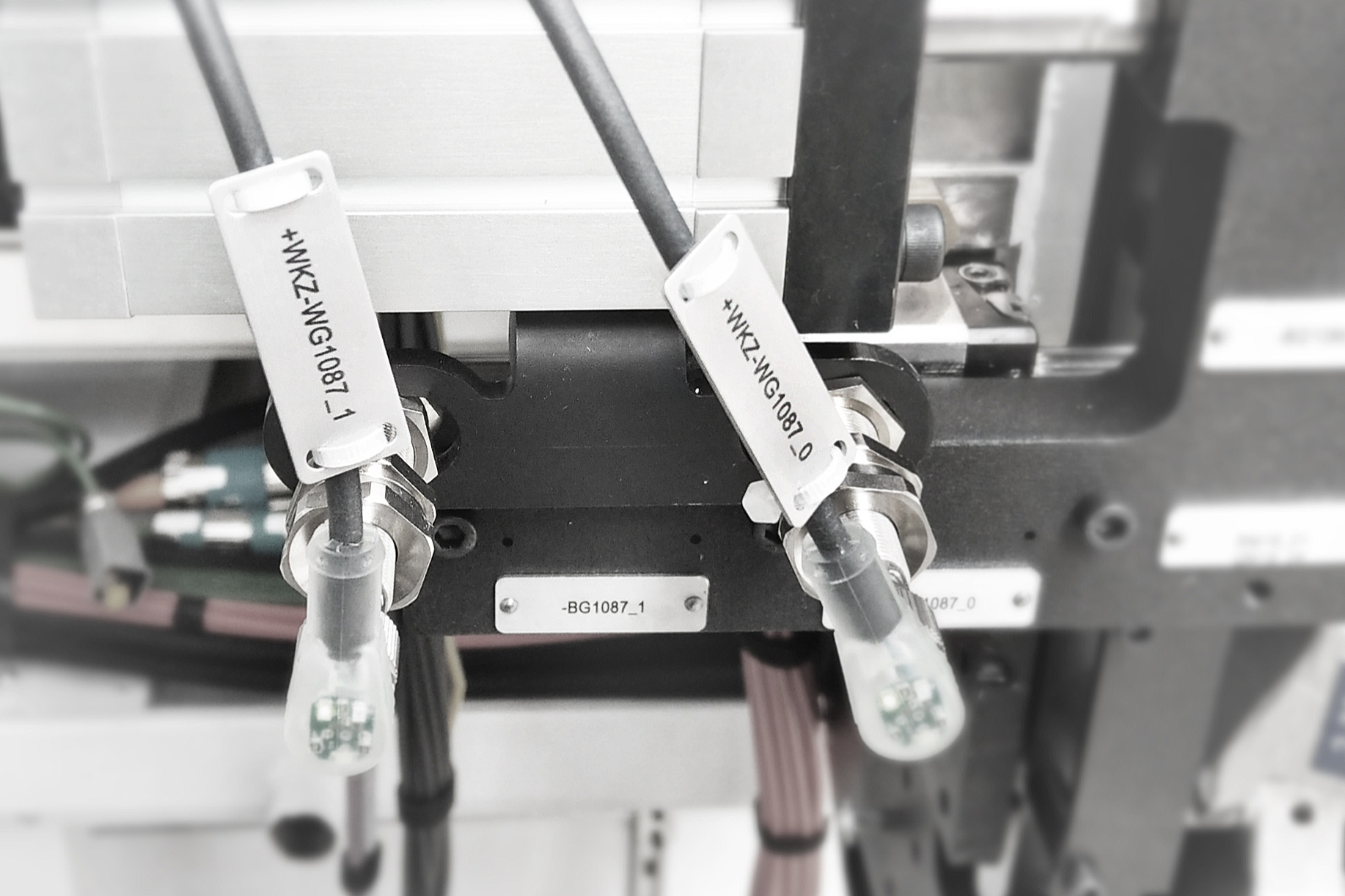 Close-up of industrial equipment with attached printolux tags, including white tags with black text and small circuit boards at the end of attached cables.