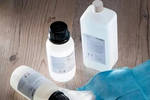 Three bottles of cleaning or chemical products and a blue cloth on a wooden surface.
