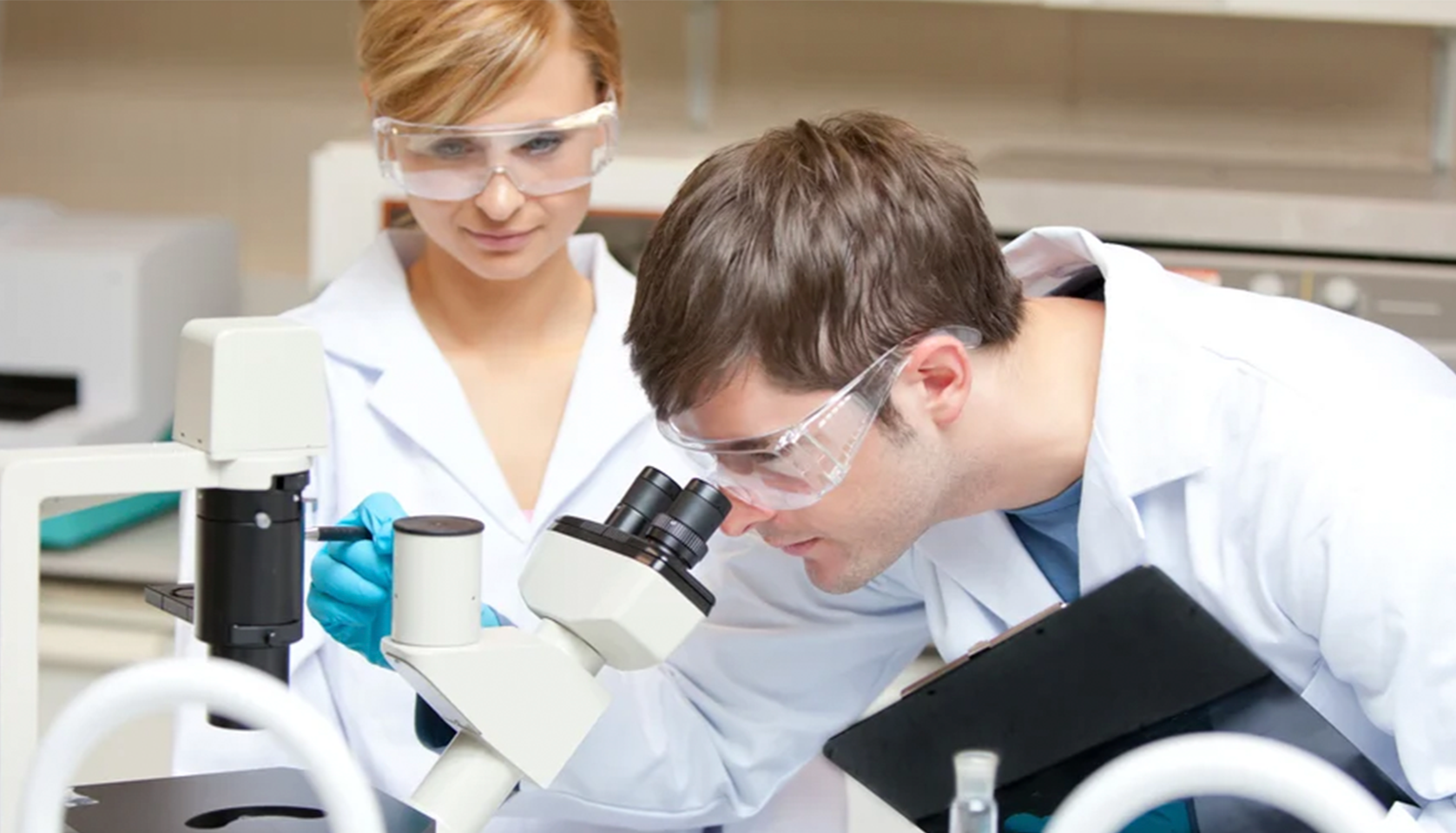 Two scientists, a woman and a man, working together in a laboratory, examining something through a microscope.