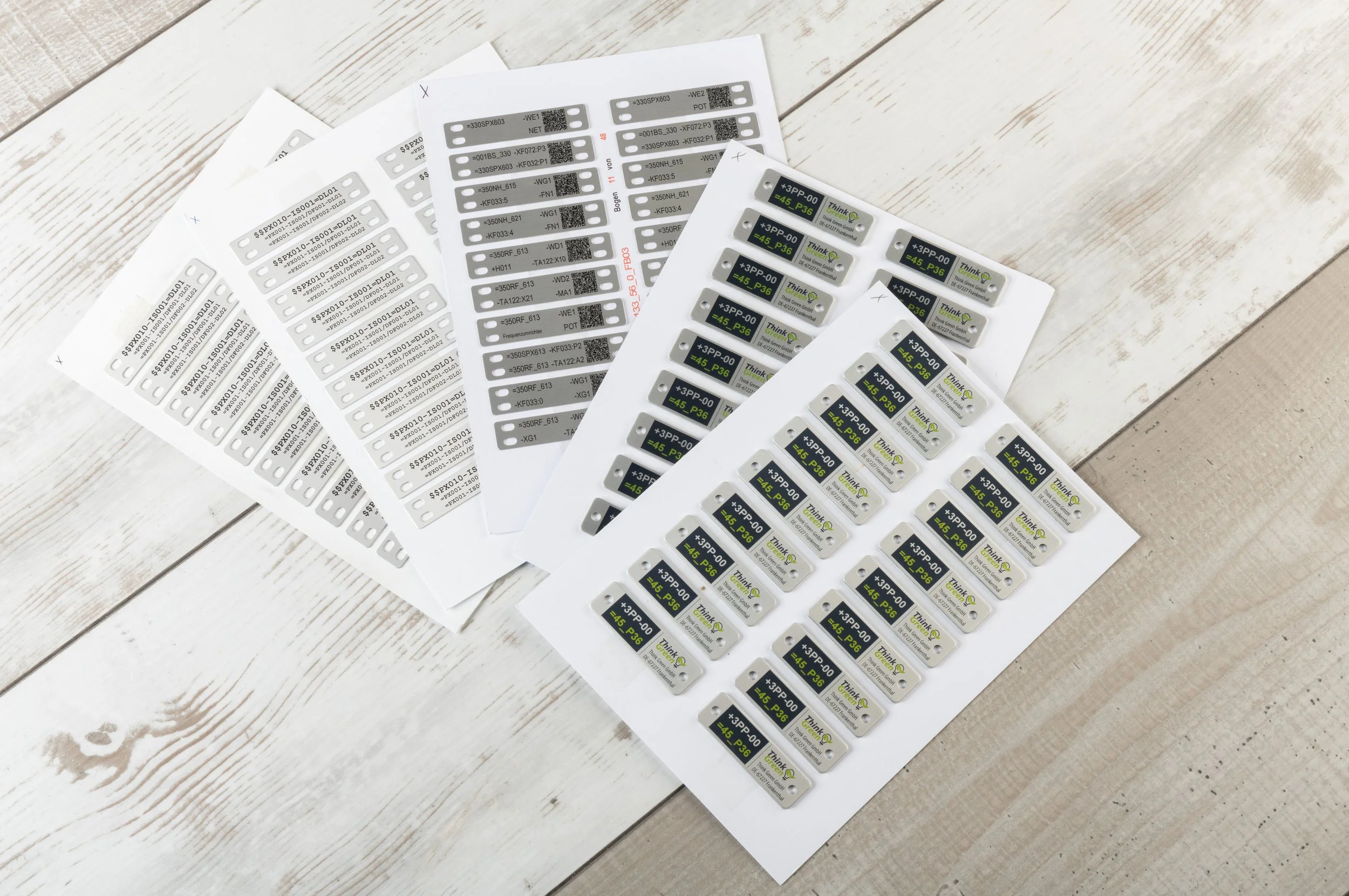 Sheets of printed PrintoLUX aluminium tags on a wooden surface.