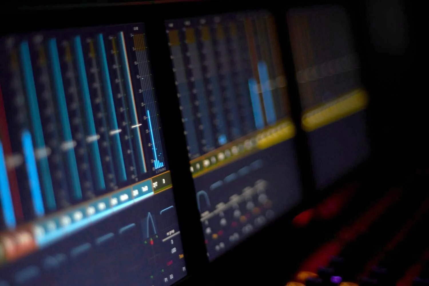 Close-up of multiple computer screens displaying audio mixing and editing software in a dark room.