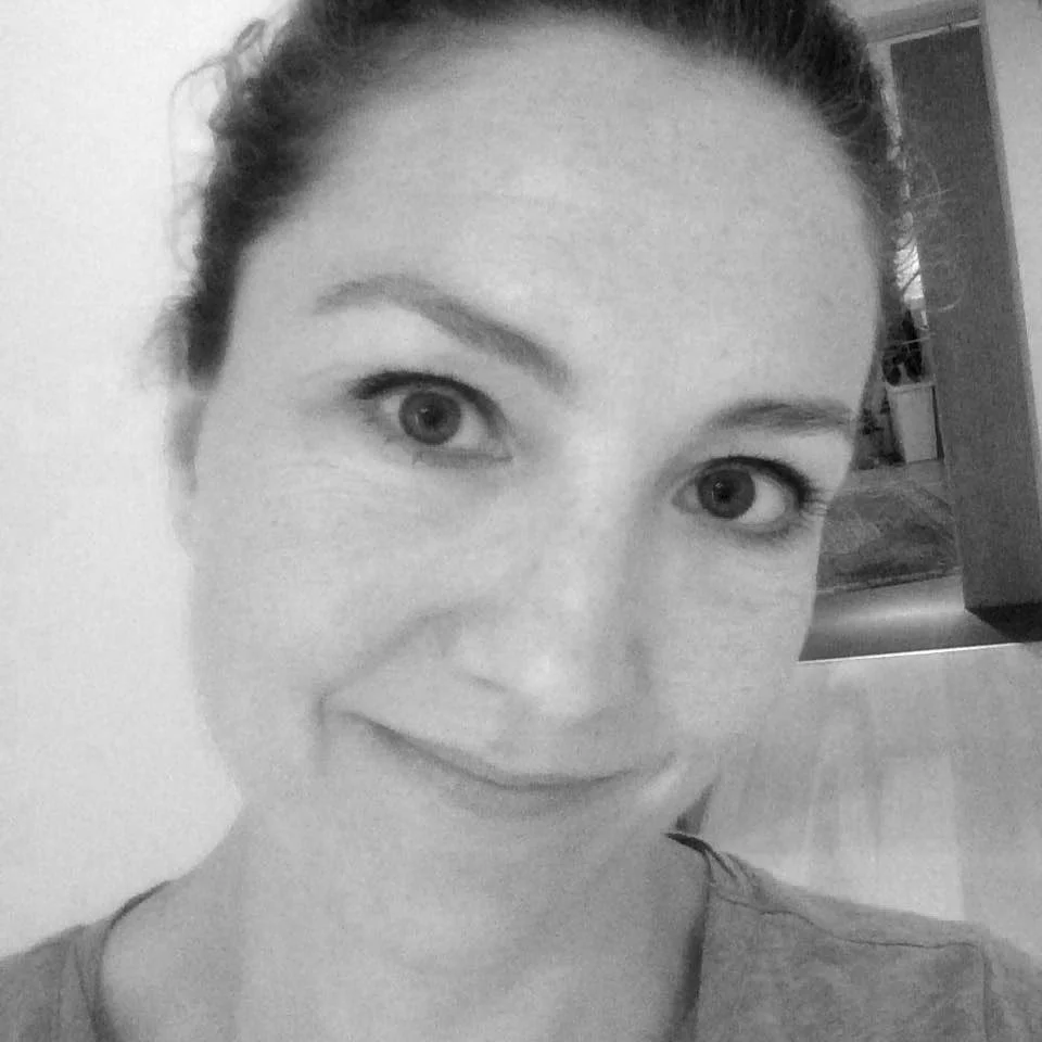 A black and white close-up photo of a smiling woman with her hair pulled back, showing her face and eyes clearly.