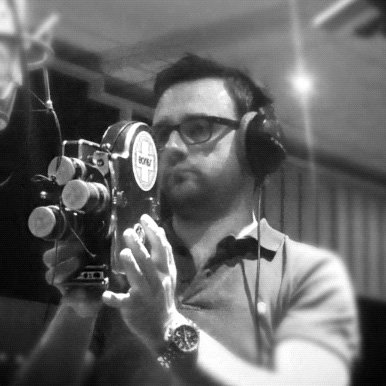 A man wearing glasses and headphones recording in a music studio with a microphone.