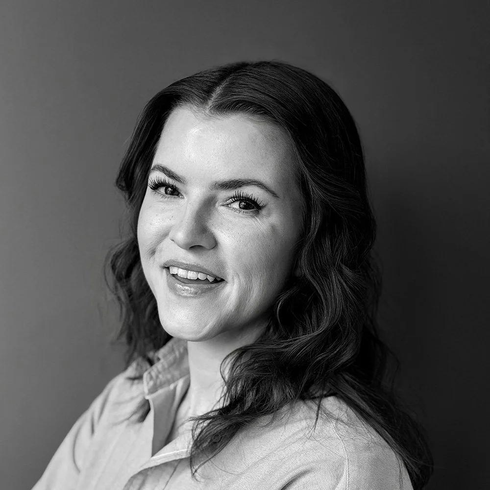 Black and white portrait of a woman with wavy hair, smiling, wearing a collared shirt, against a plain background.