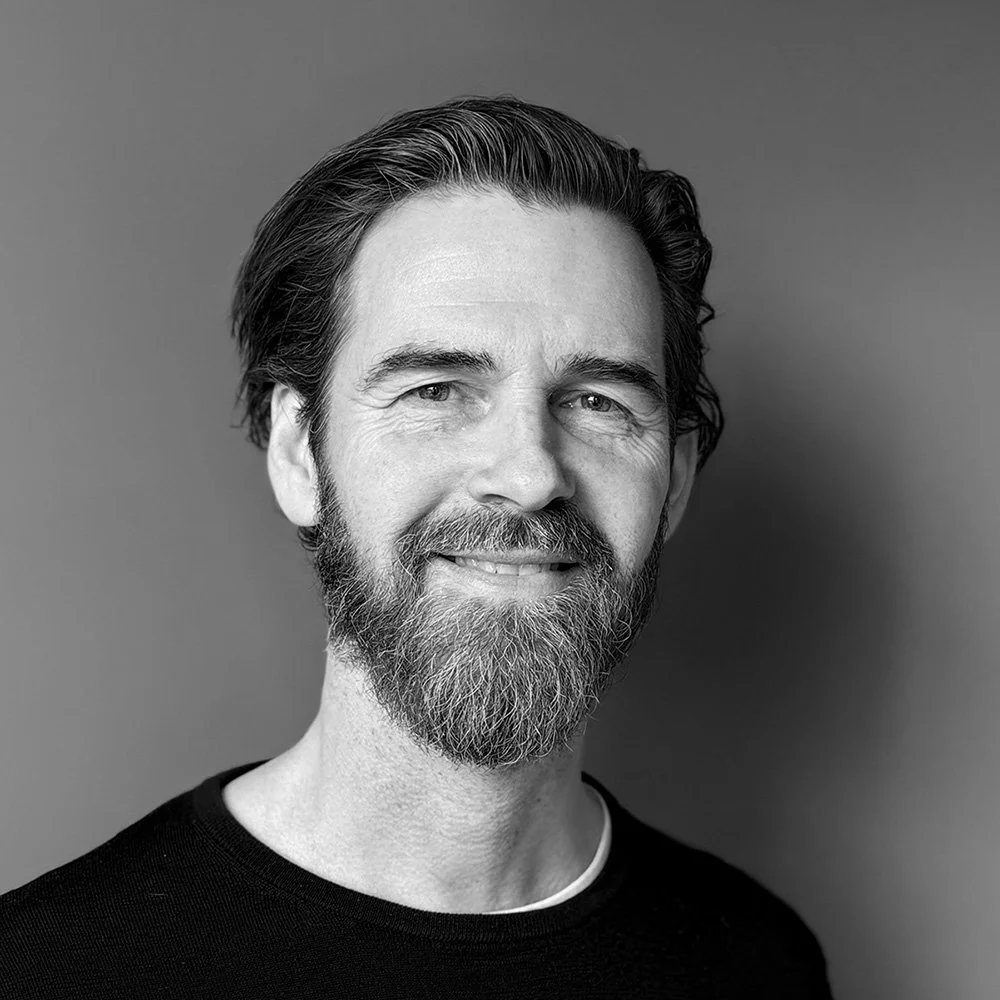 Black and white portrait of a middle-aged man with a beard, smiling, against a plain background.