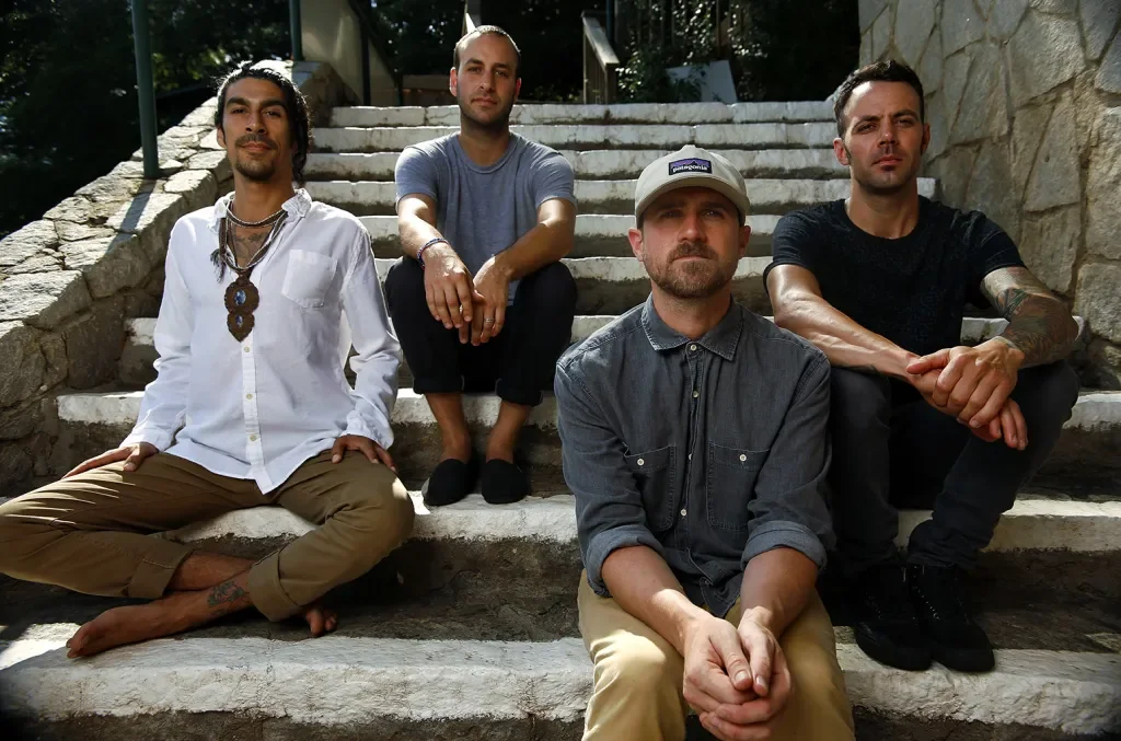 Four men sitting on outdoor stone stairs, with trees and a building in the background, posing for a photo.