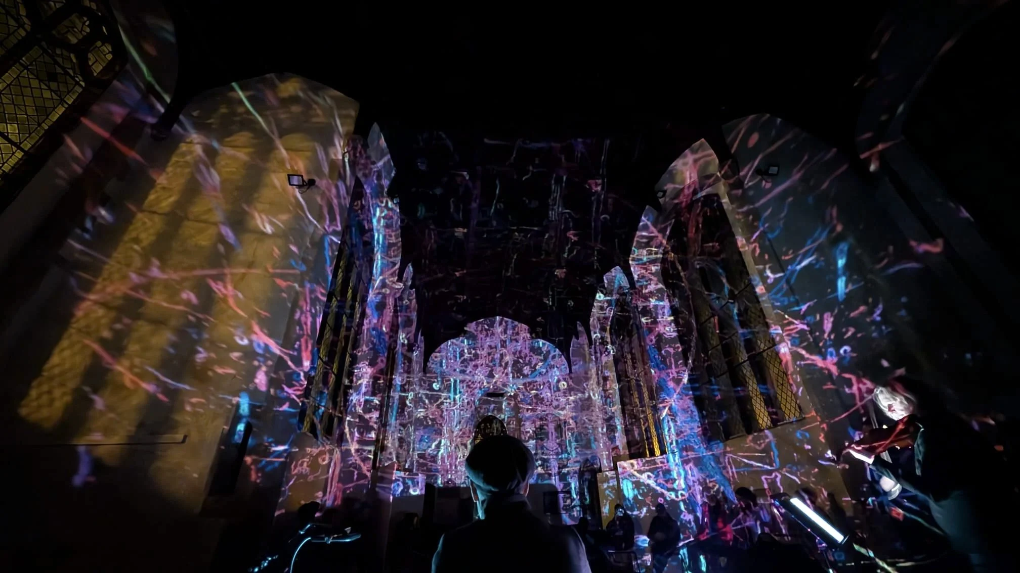Dark room with colorful, abstract light projections on walls and ceiling, creating a vibrant, immersive visual display.