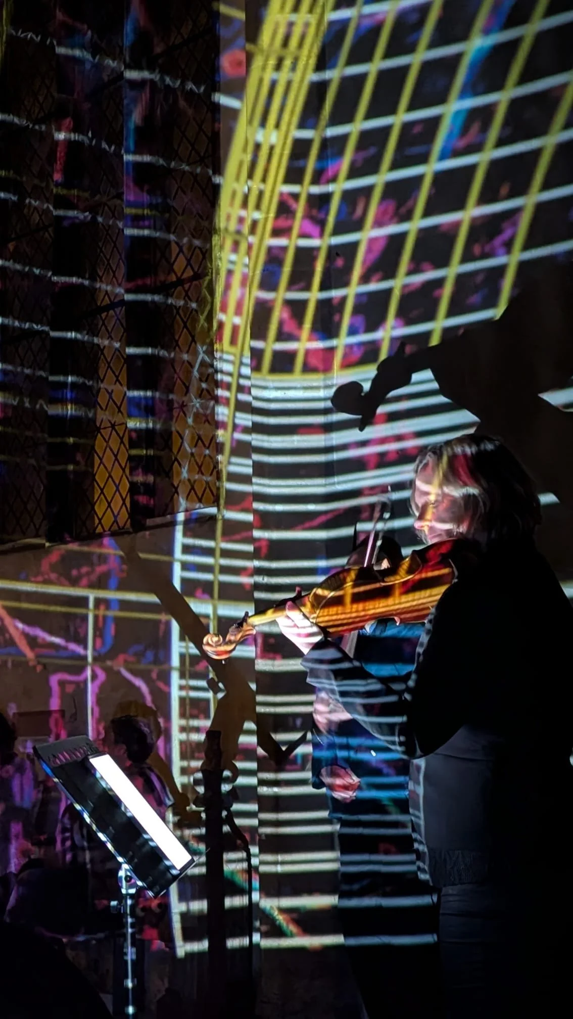 A person playing violin in front of a colorful digital projection displaying abstract patterns and lines.