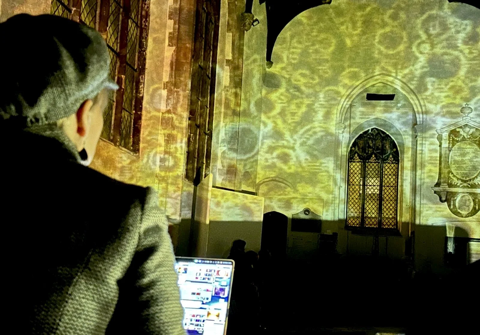 Person watching a projection of an ornate church interior on a wall, with a laptop open in their lap.