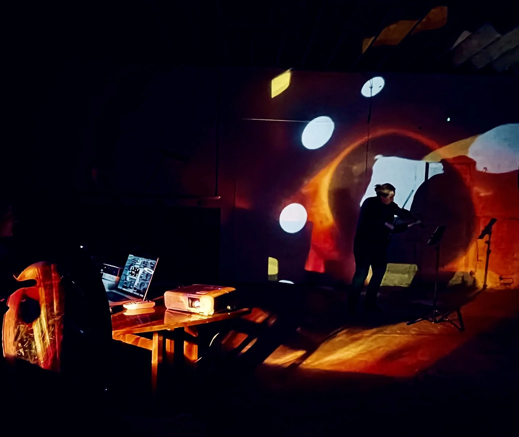 Dark indoor scene with abstract colorful lights and a person working on a laptop at a table, with some electronic devices and books nearby.