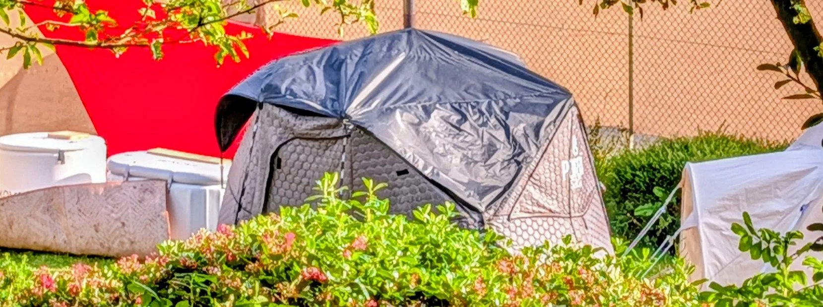 Black PortaSauna tent & white cold plunge baths surrounded by foliage.