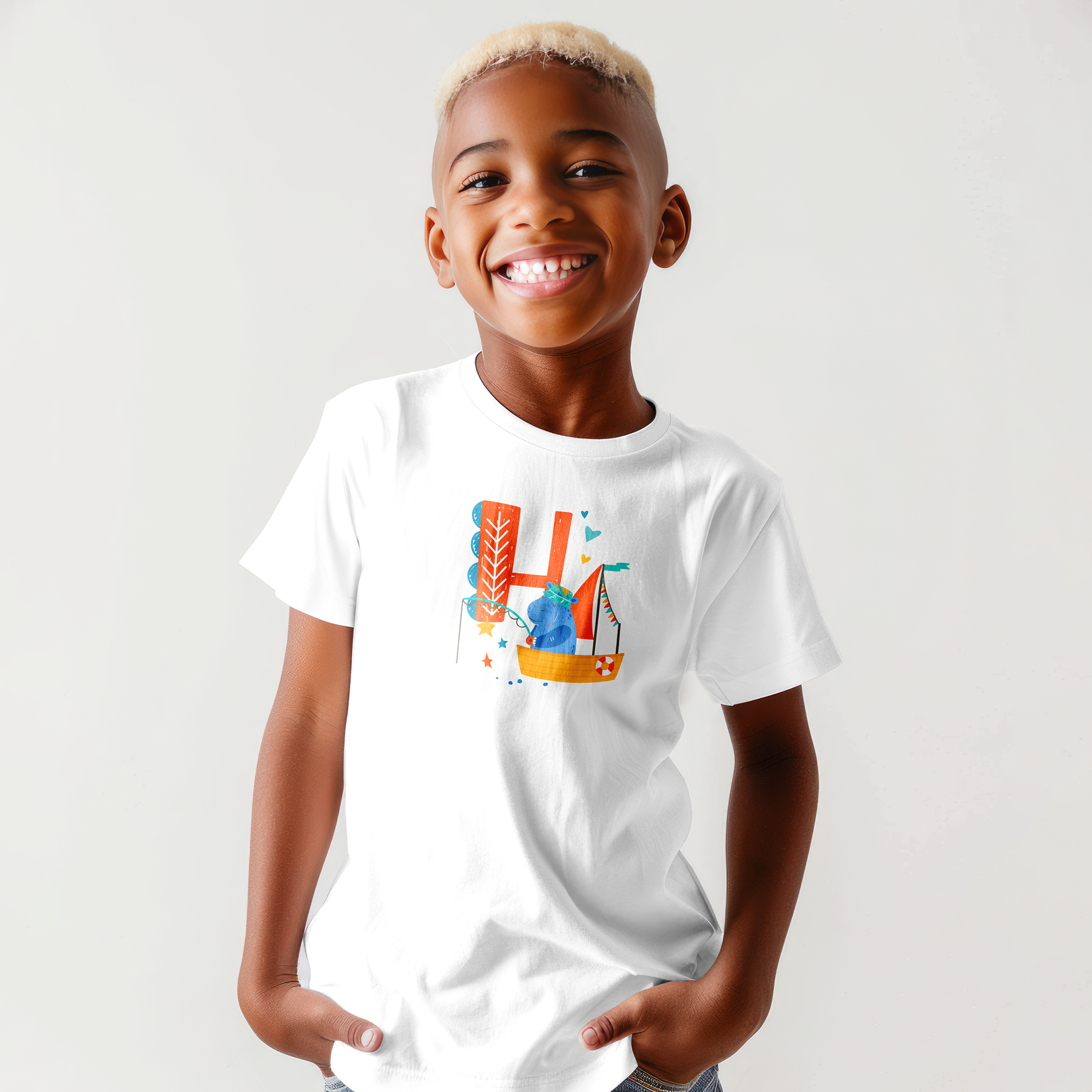 A smiling young boy with short, bleached hair wearing a white t-shirt with colorful graphics, standing against a plain white background.