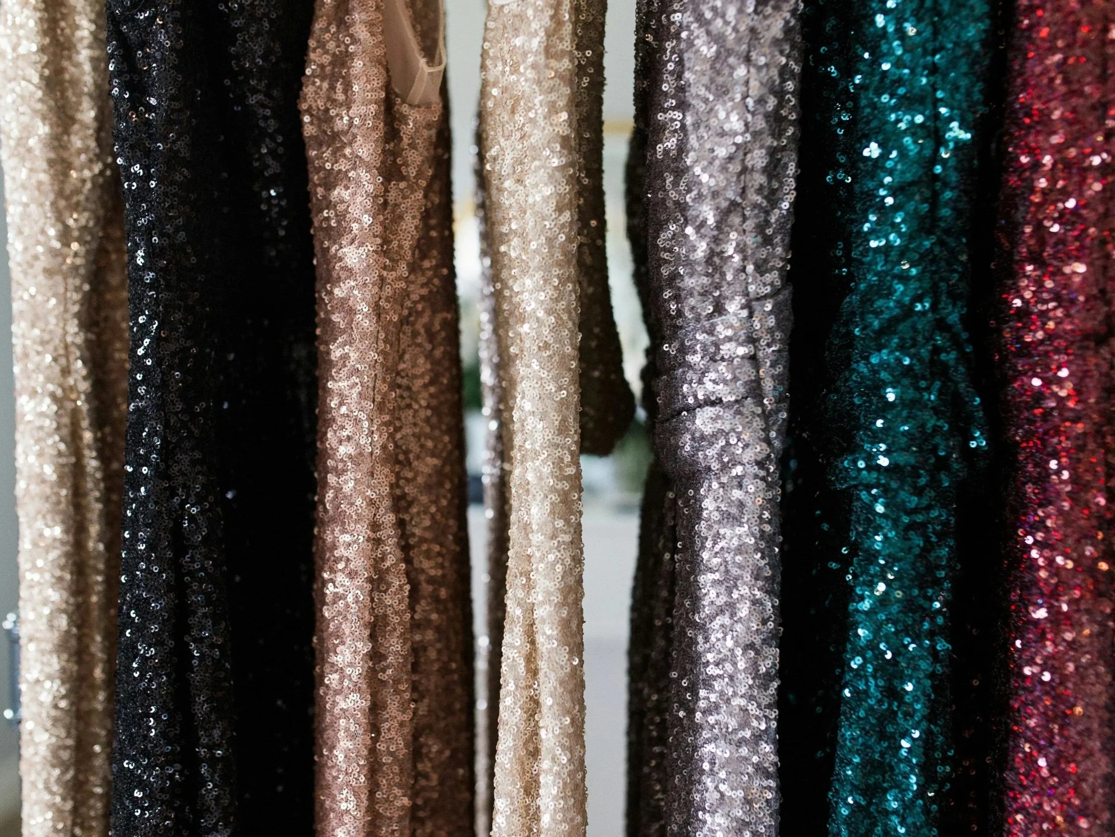 Close-up of hanging sequin fabric in various colors, including gold, black, beige, silver, turquoise, and red.