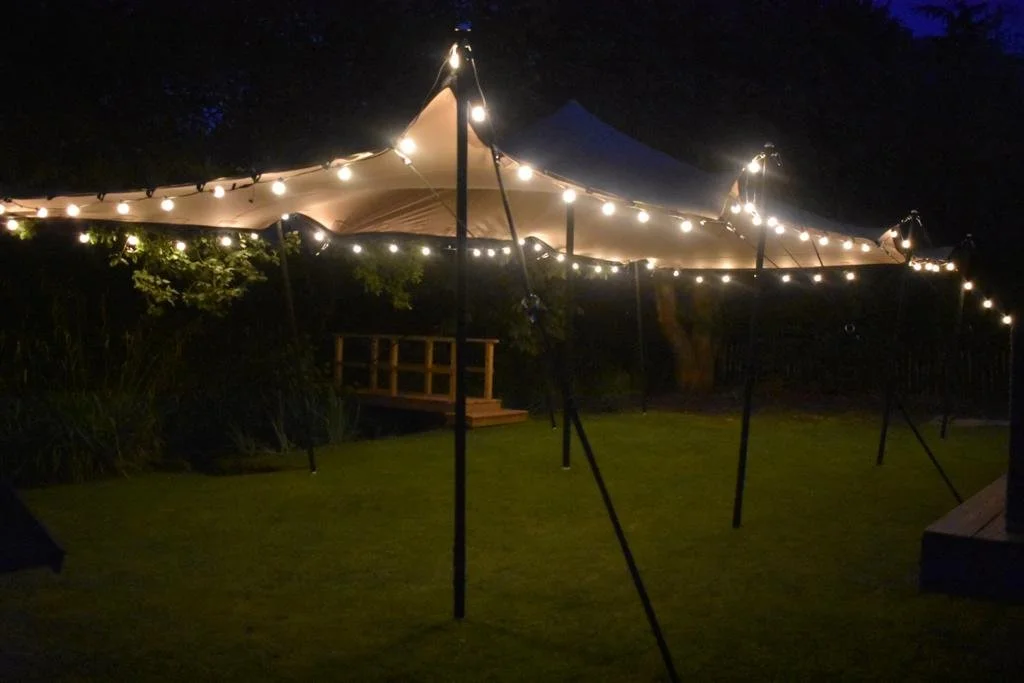 Outdoor tent with string lights illuminated at night on a grassy area.
