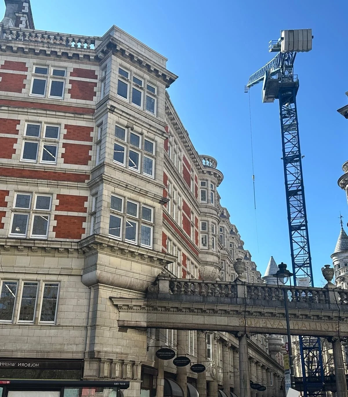 A historic multi-story building with red brick and beige stone architectural details, with a construction crane nearby against a clear blue sky.