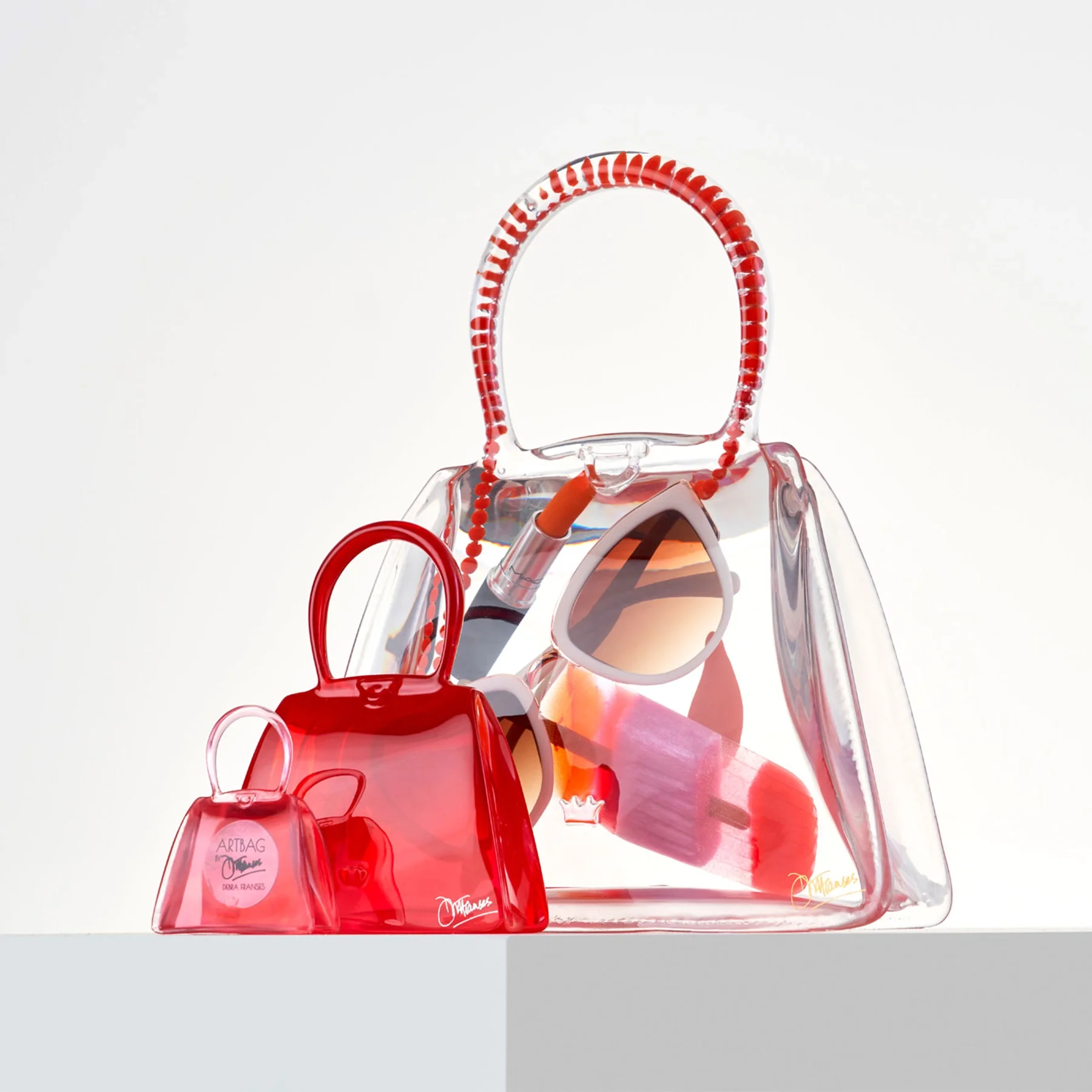 Collection of transparent red handbags and sunglasses on a white surface.