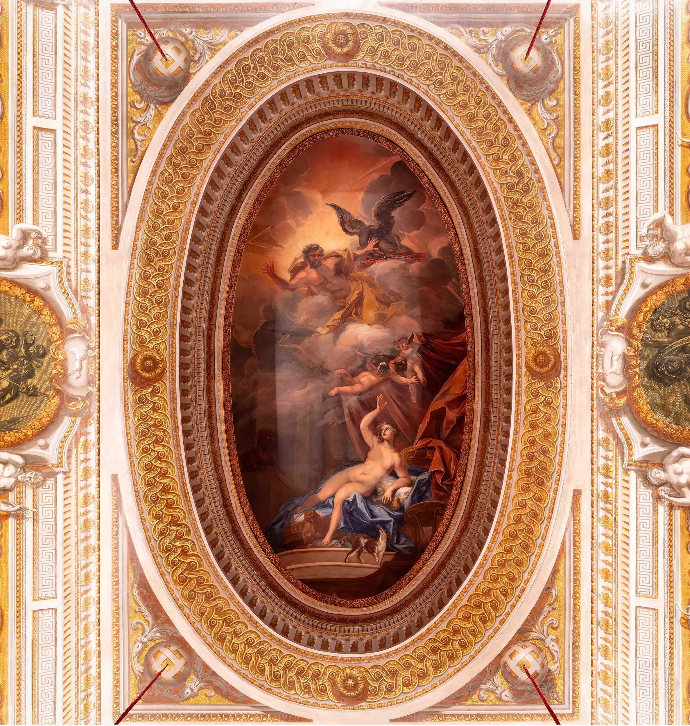 Ornate ceiling with gold, white, and red decorative elements, featuring a central painting depicting mythological scene with a winged figure, clouds, and a reclining woman.