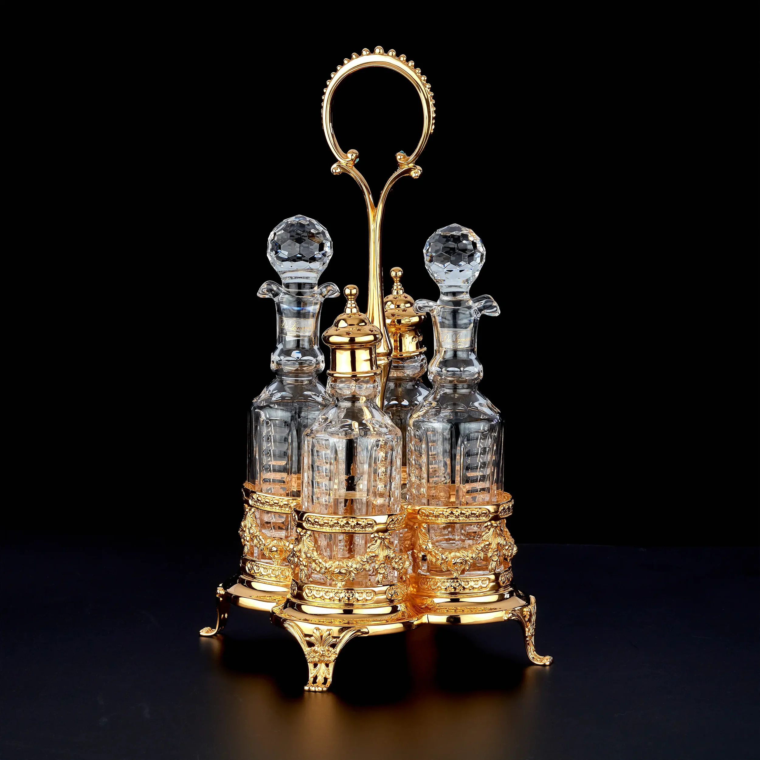 A luxurious gold-colored jewelry stand with intricate designs, holding several pieces of jewelry, including a large ring with a textured band, two crystal jewelry containers, and various gold bangles, all set against a black background.