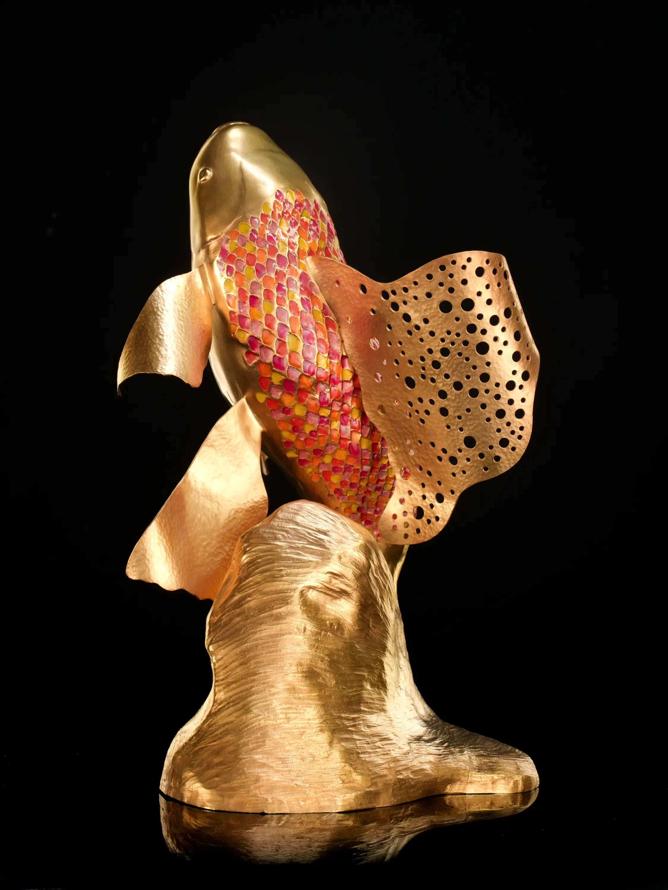 Gold-colored sculpture of a woman's side profile with a floral-like structure resembling a headpiece, against a black background.