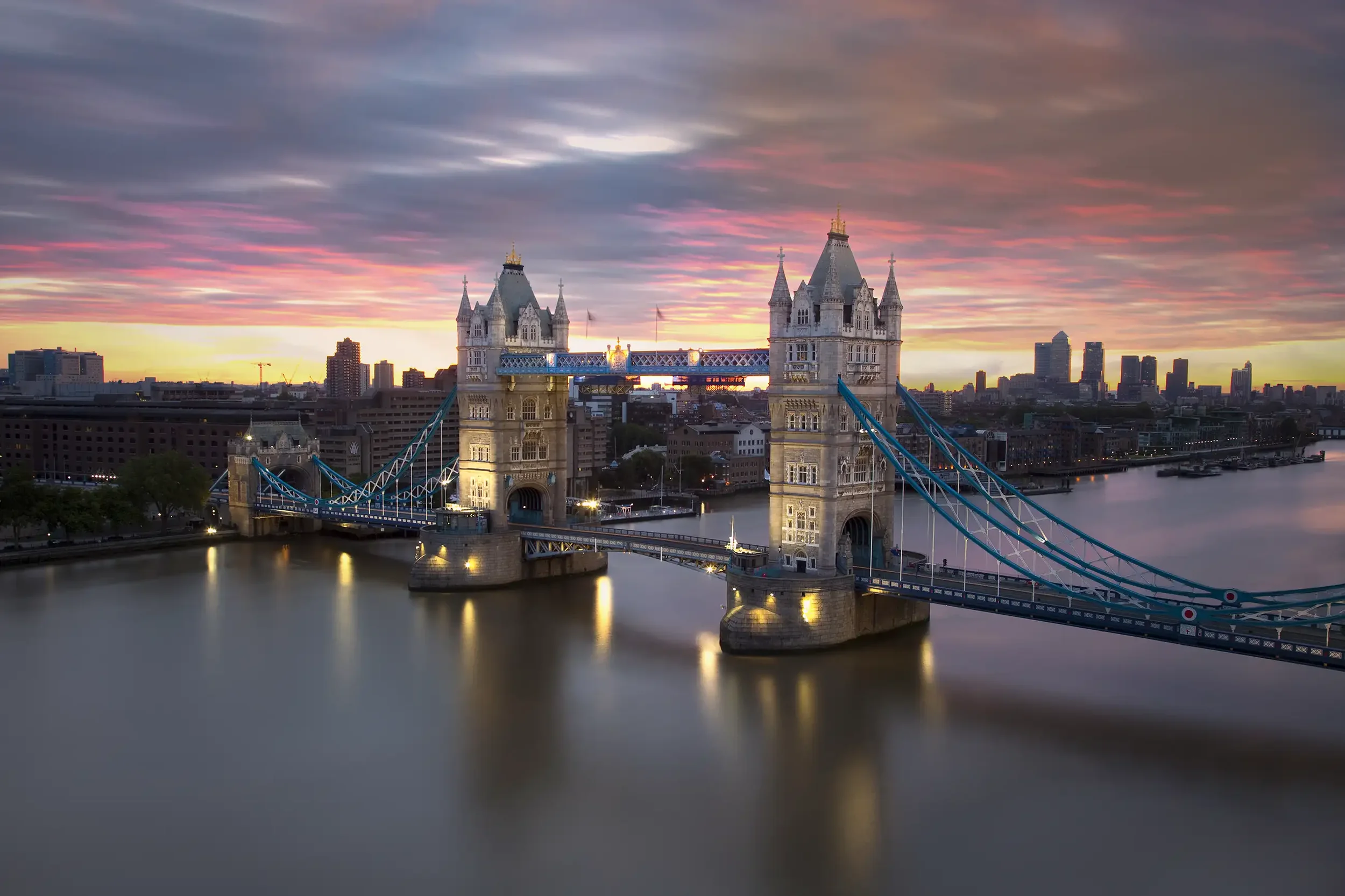 Sunset view of Tower Bridge over the River Thames in London with colorful sky and city skyline in the background.