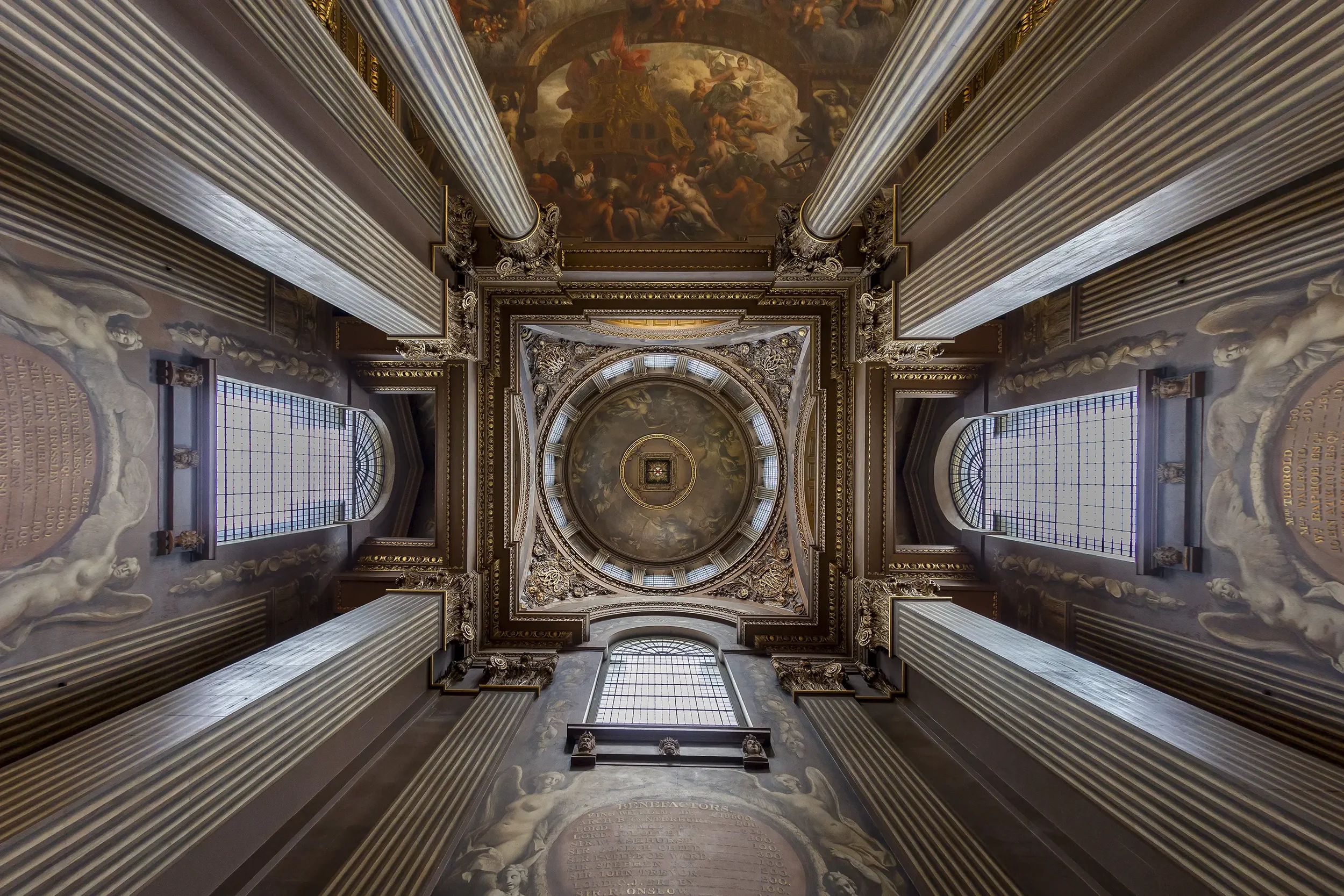 Looking up at the ornate ceiling of a grand building with columns, intricate gold accents, and large paintings.