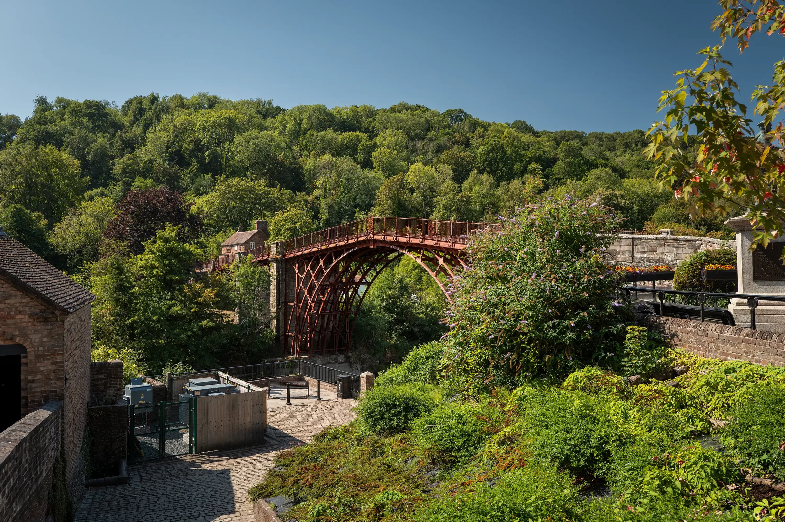 A scenic view of a red arch bridge over a lush green valley with trees on a clear sunny day.