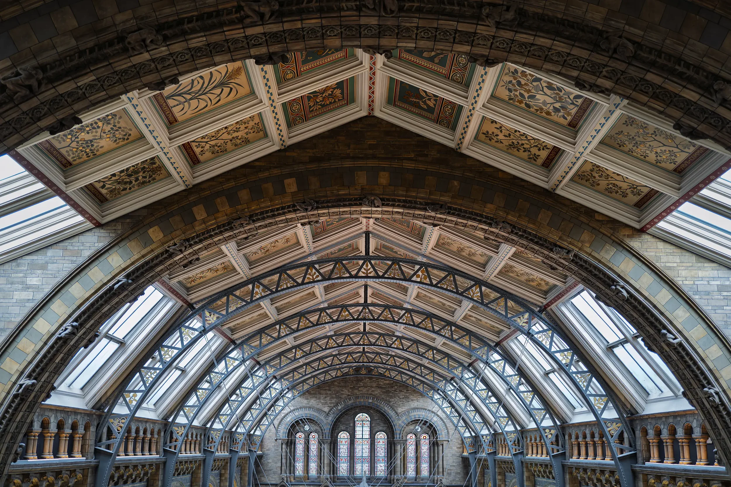 Interior view of a historic building with ornate vaulted ceiling, painted decorative panels, and stained glass windows.
