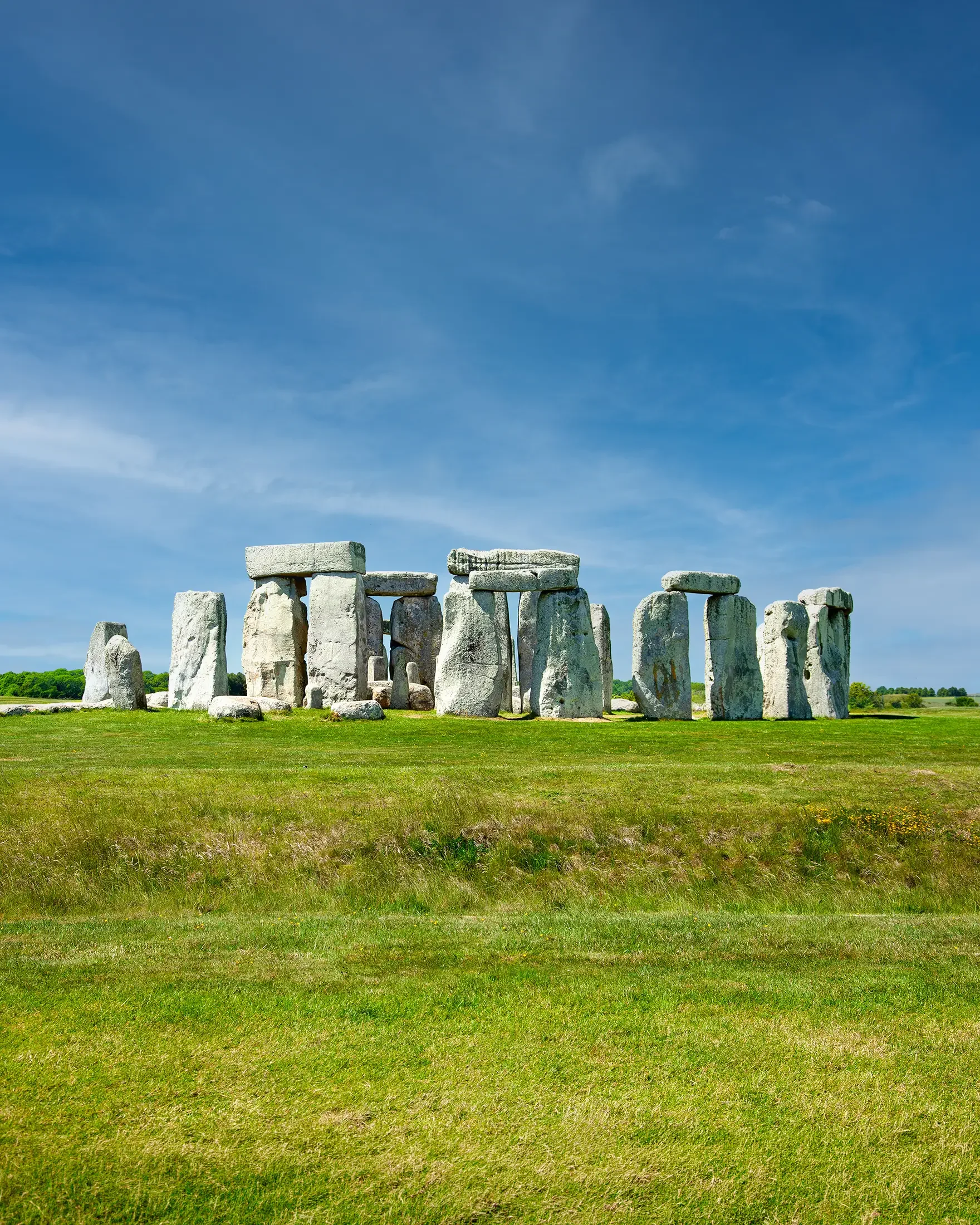 The image features Stonehenge, a historic prehistoric monument located in England, with a clear blue sky and lush green grass surrounding the stone circle.