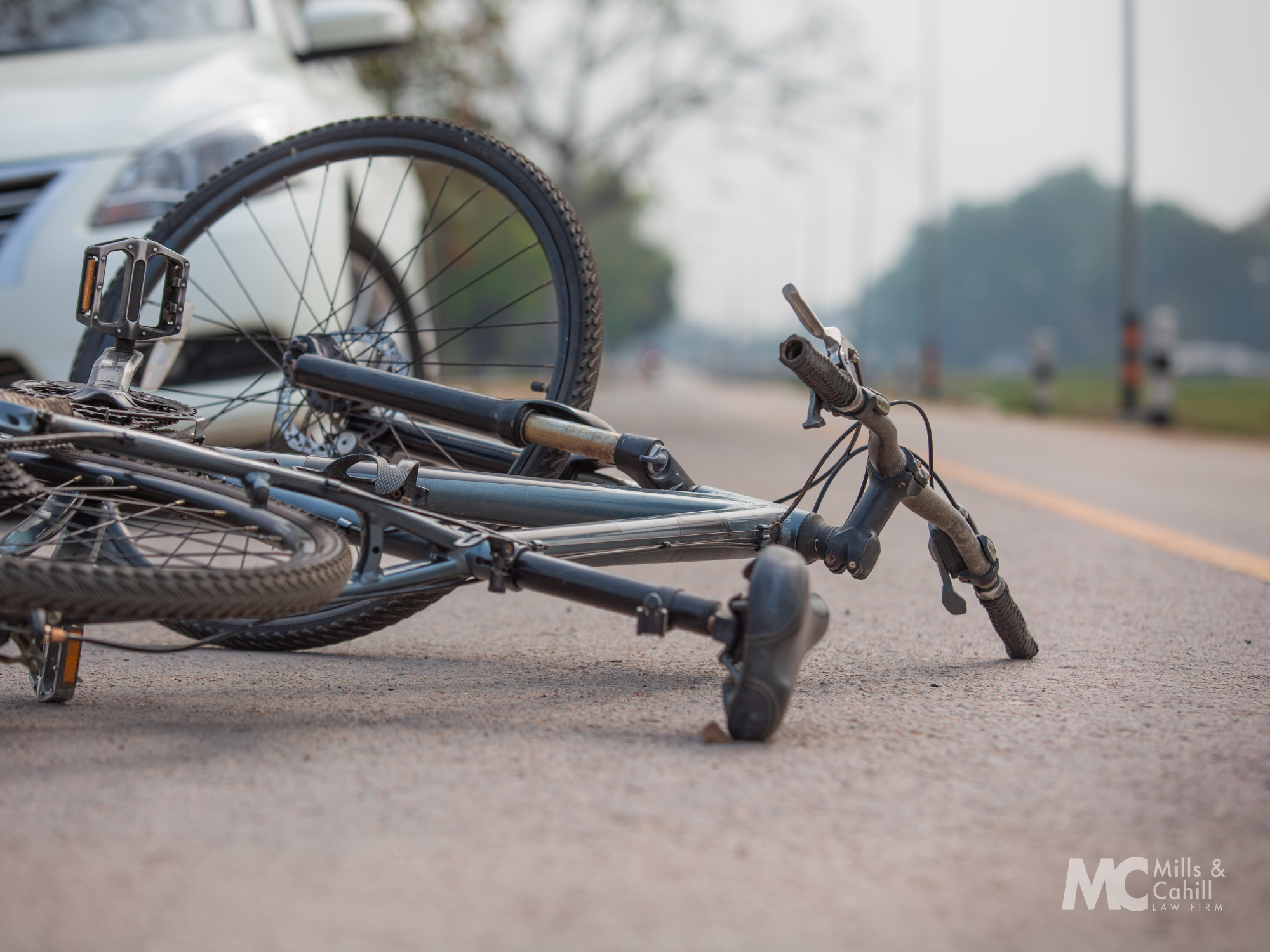 Fallen bicycle lying on the road with a car in the background.