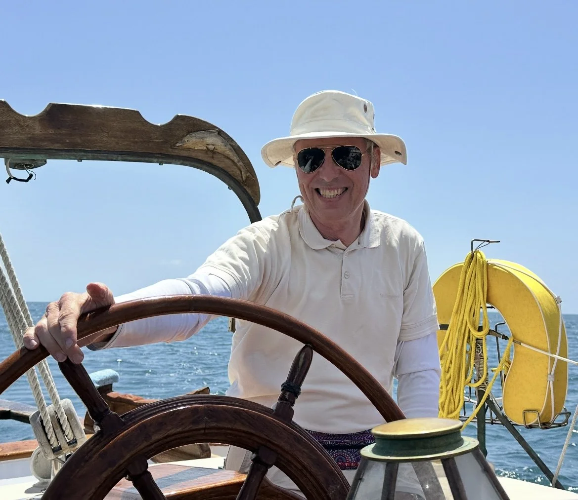 Dirk Langer wearing sunglasses and a white hat sailing a boat on a sunny day.